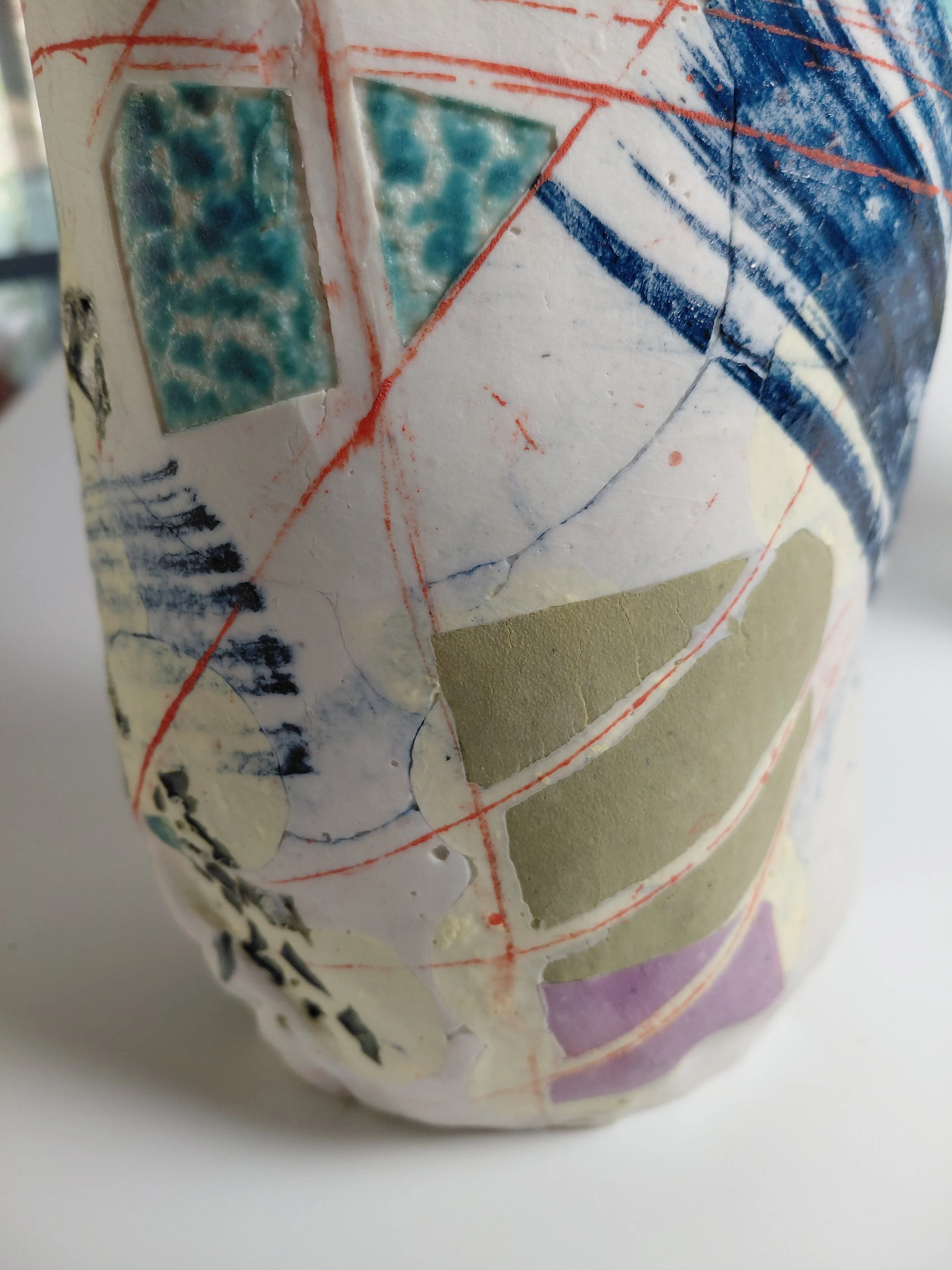 Close-up of a textured surface with painted geometric shapes and lines, including rectangles, triangles, and curved lines in various colors like blue, green, purple, and red.