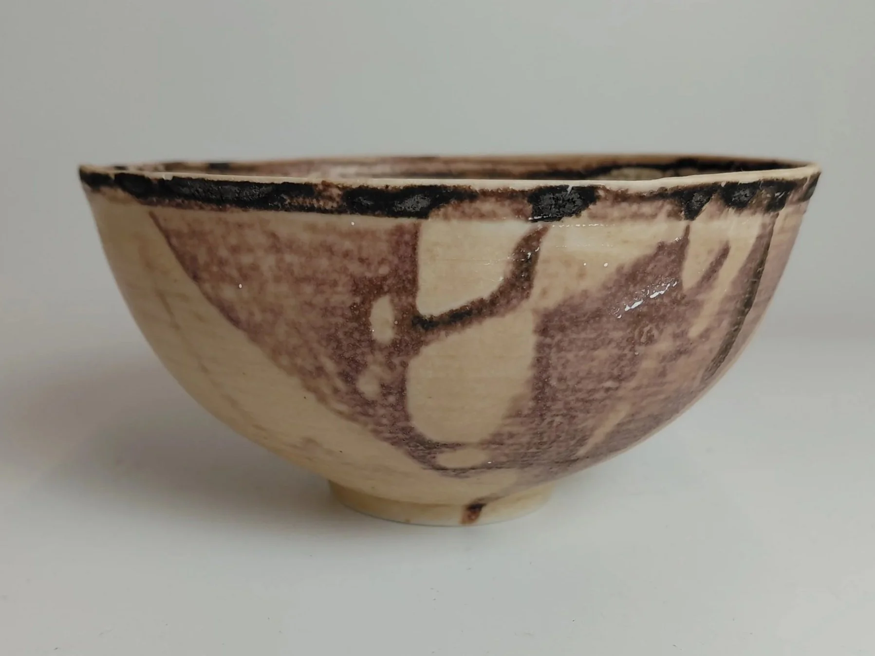 Close-up of a ceramic bowl with a cream-colored background and dark brown abstract patterns.
