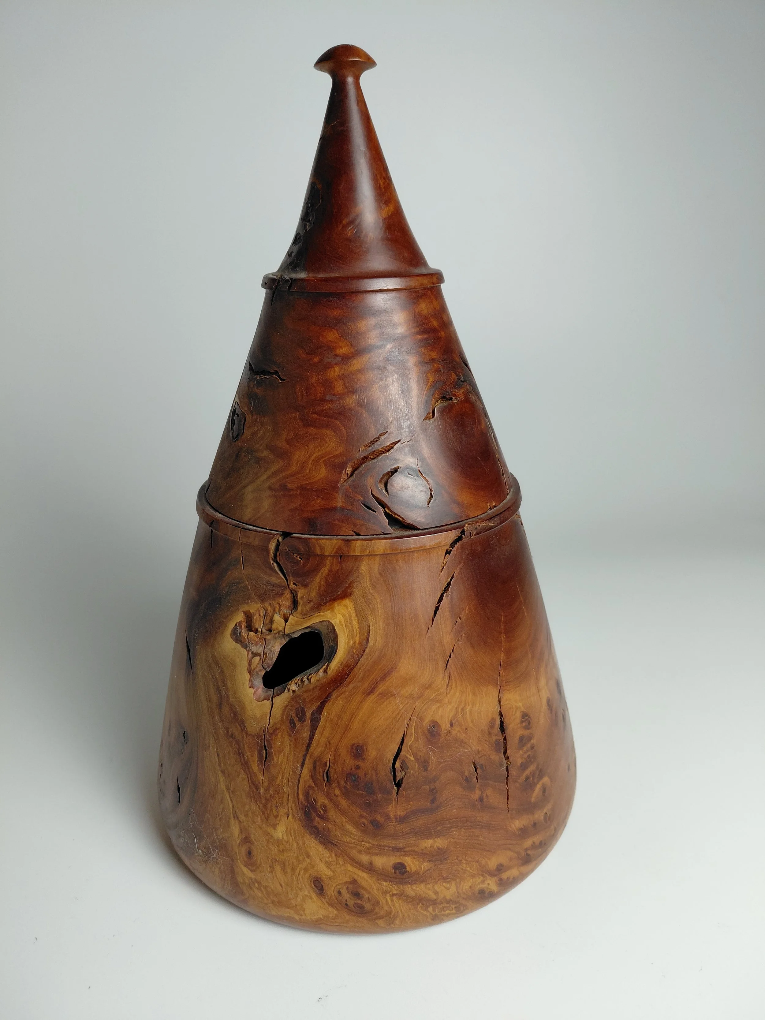 A wooden vuvuzela with a natural wood finish and visible wood grain, showing cracks and knots.