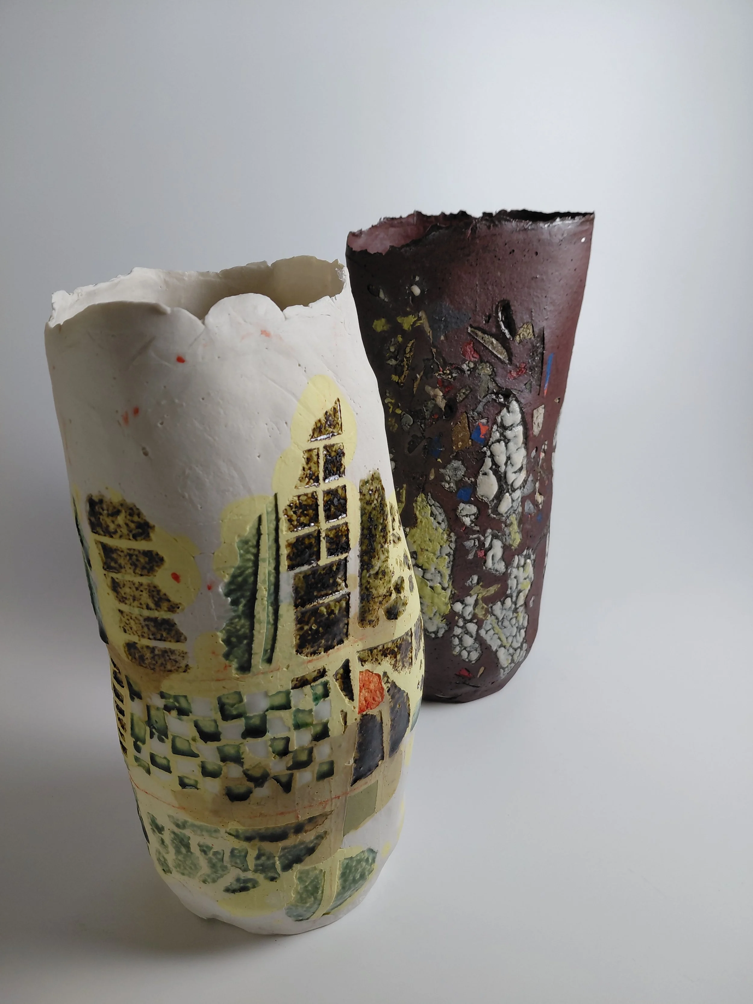 Two broken decorative paper lanterns, one white with a landscape scene and the other dark with an abstract pattern, standing upright on a white surface against a plain white background.