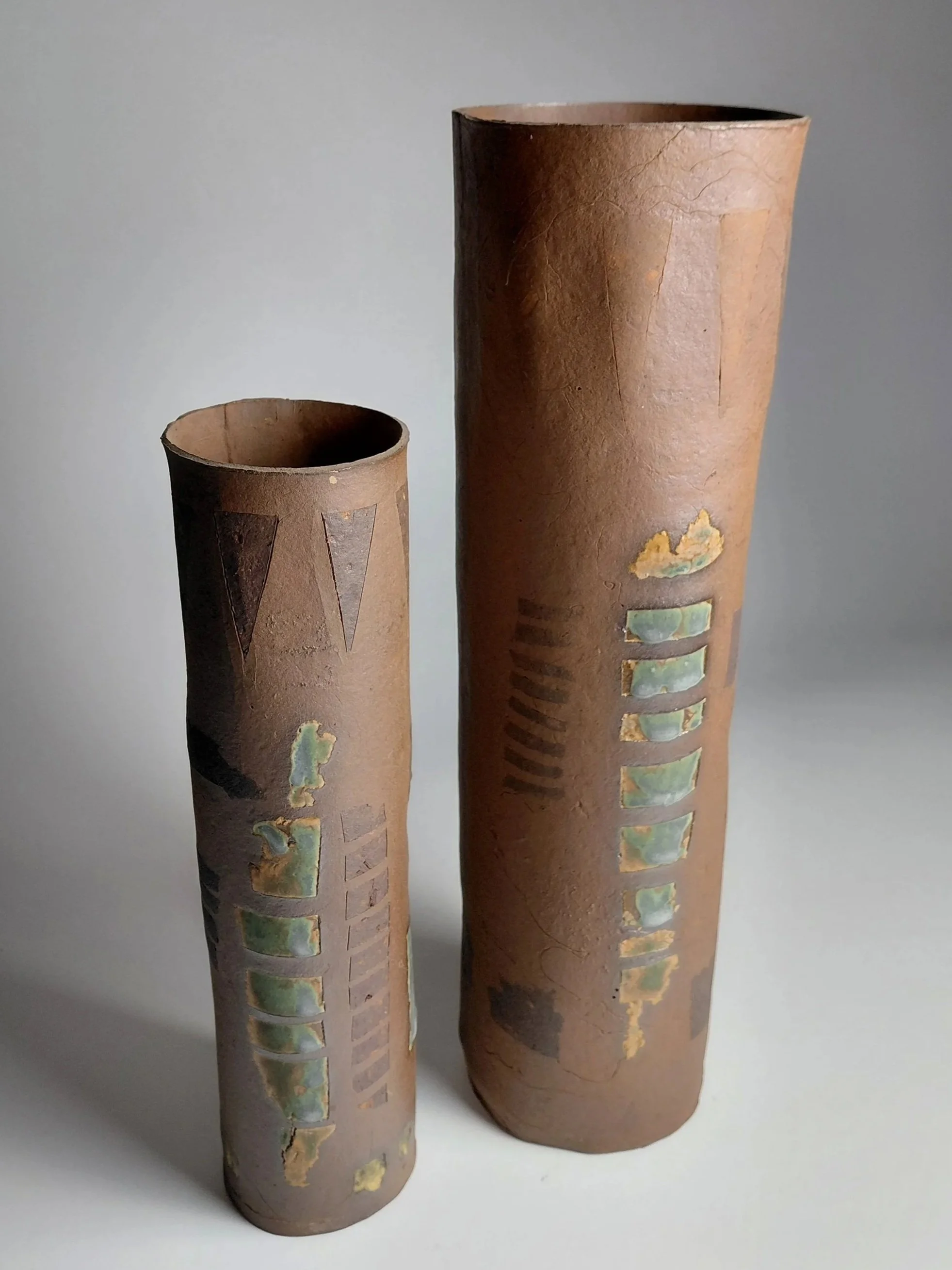Two tall, cylindrical, textured terracotta planters with decorative inlays on a white background.