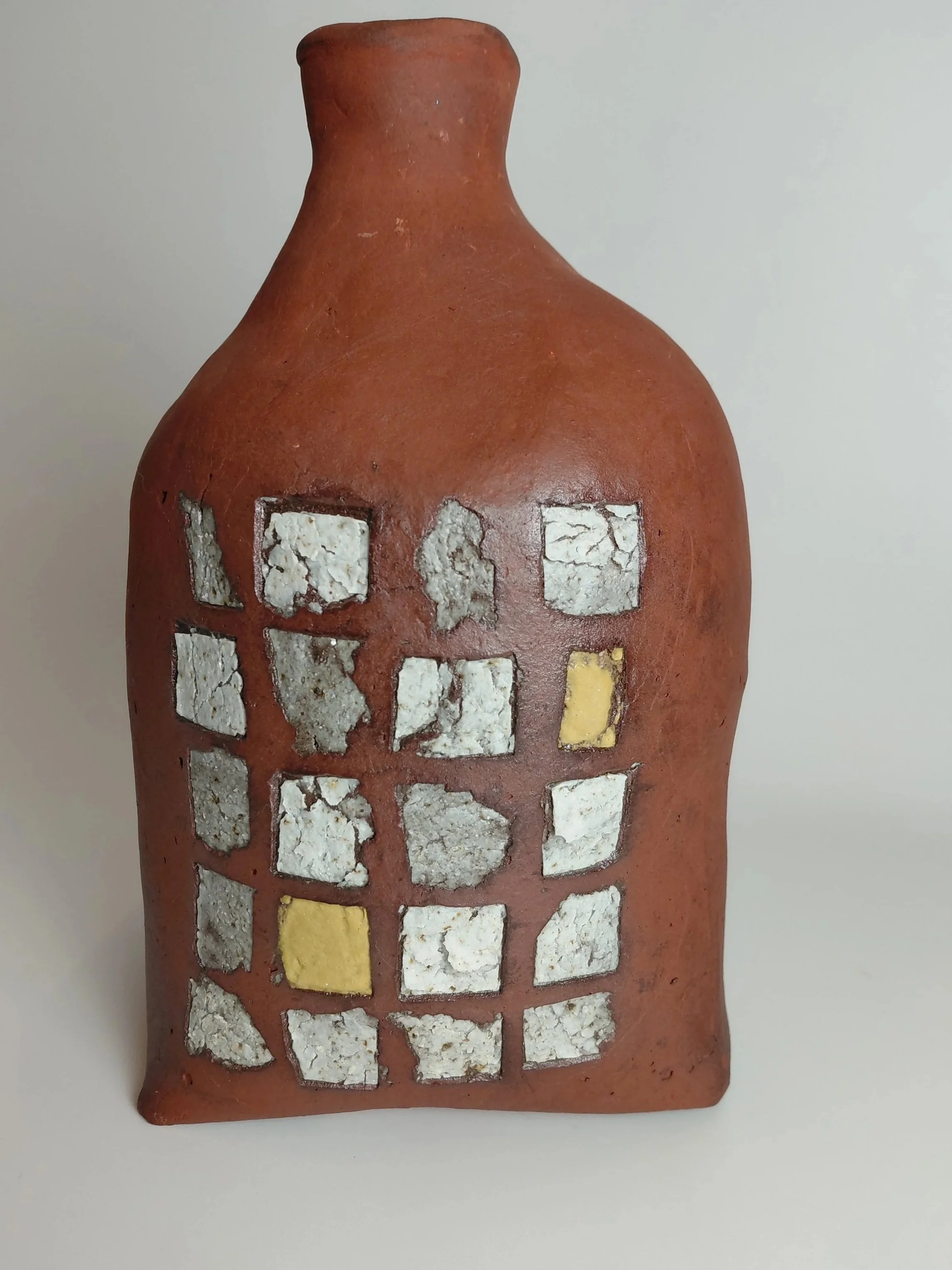 A decorative ceramic vase with a brick-red color and irregularly placed white and yellow mosaic tiles on its surface.