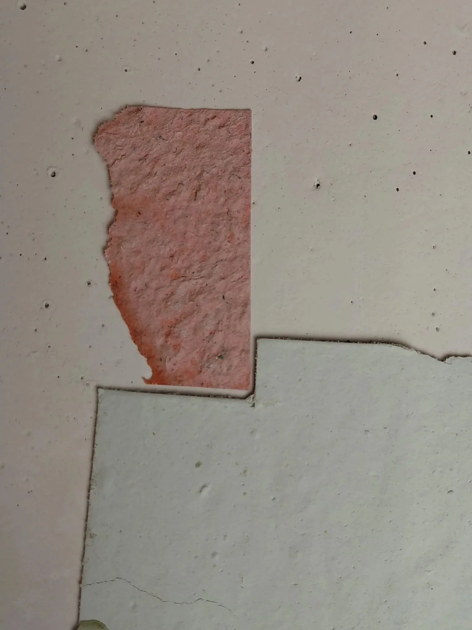 Close-up of a damaged and cracked section of a beige wall with peeling paint and exposed pink drywall.