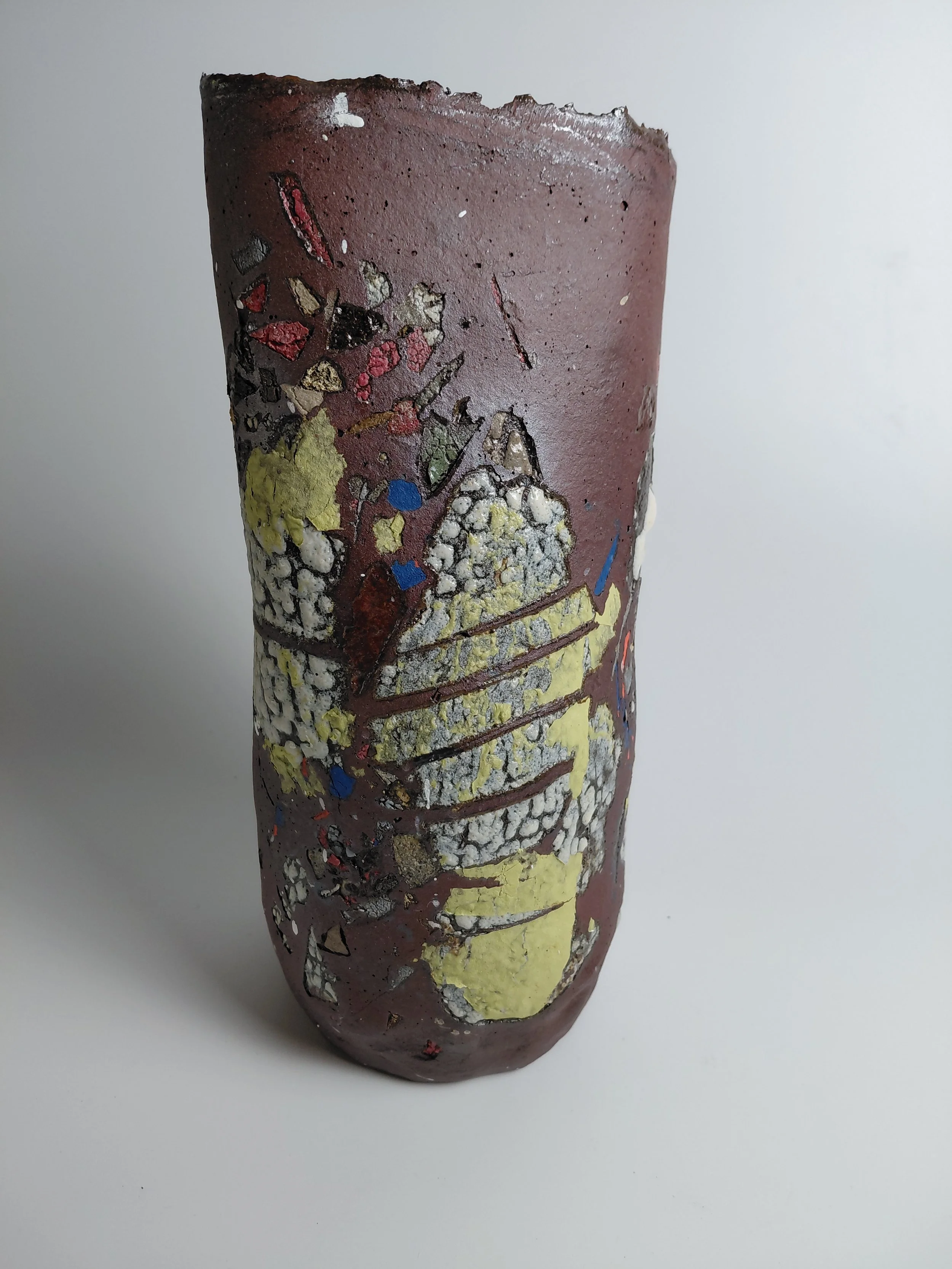 Close-up of a piece of broken ceramic or pottery with a colorful, abstract design in red, yellow, black, blue, and white on a white background.