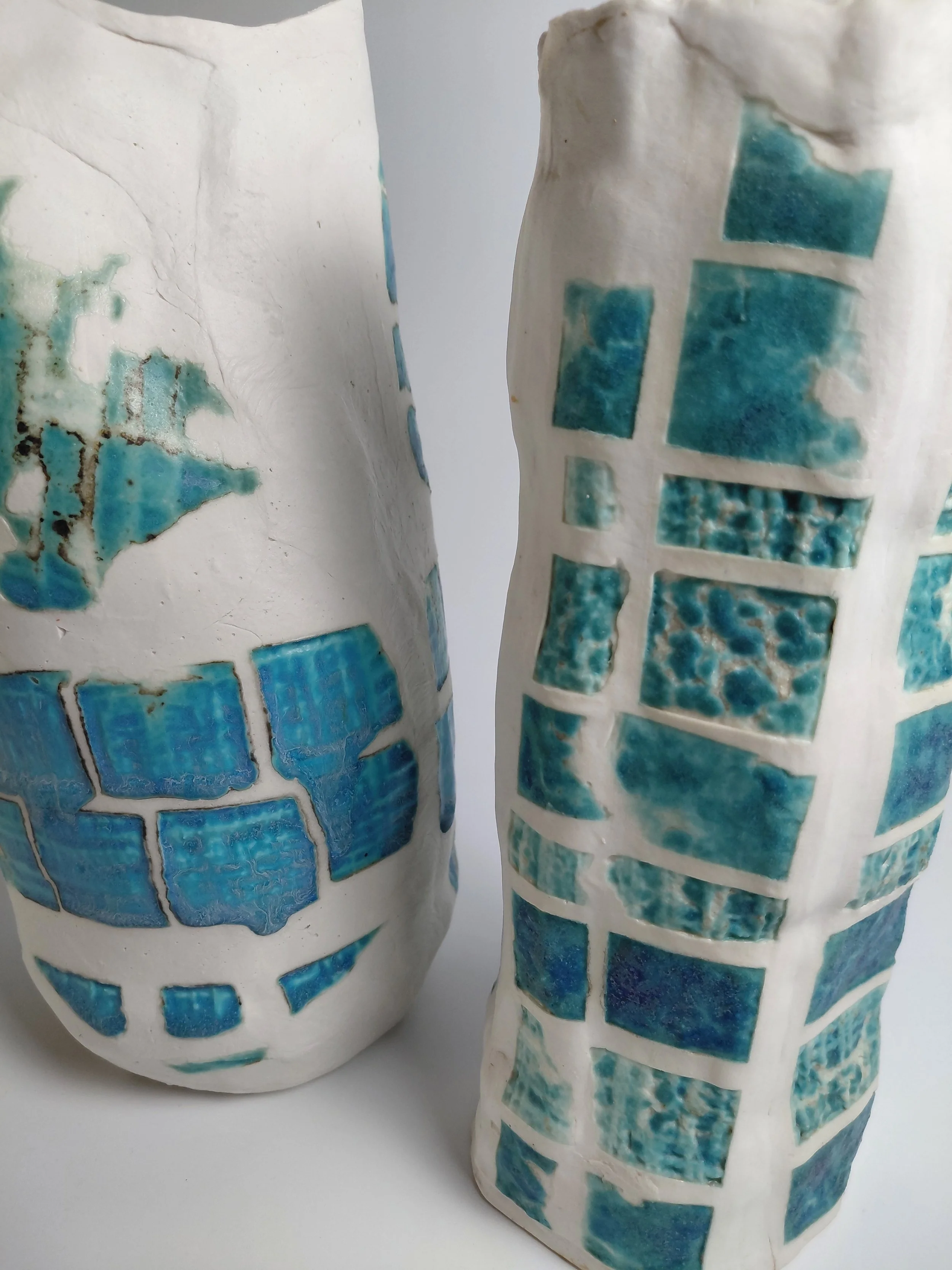 Close-up view of two ceramic vases with mosaic patterns in shades of blue and turquoise on a white background.