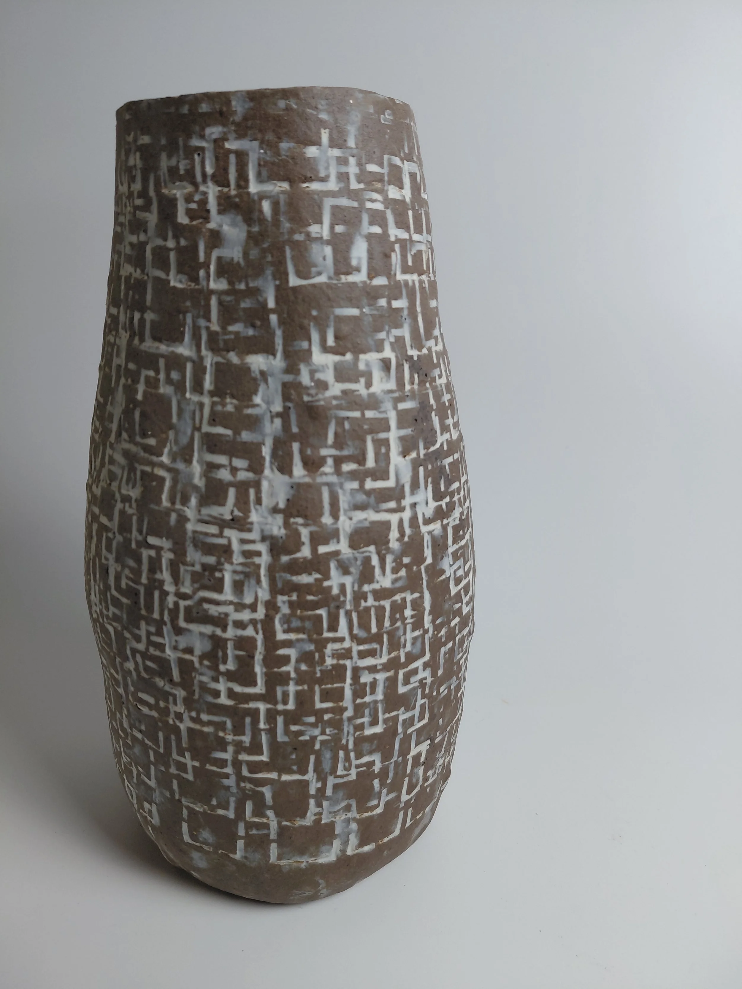 Ceramic vase with a geometric maze pattern in brown and white, placed on a white surface against a plain gray background.