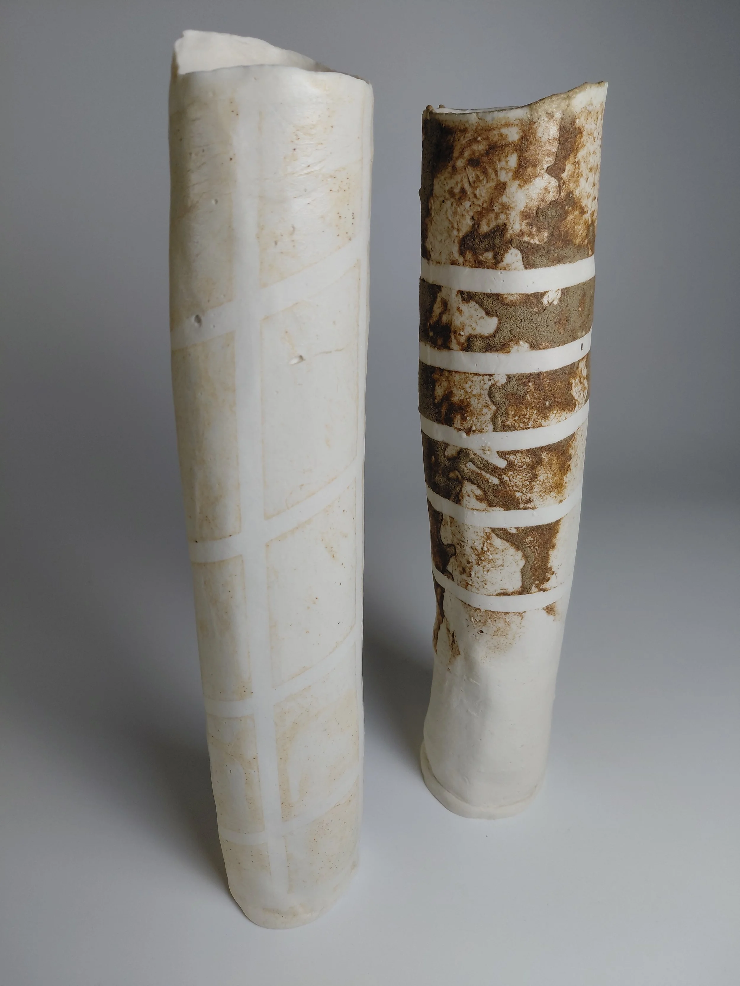 Two cylindrical bones, one white and aged, the other brown and aged, standing upright on a light surface.