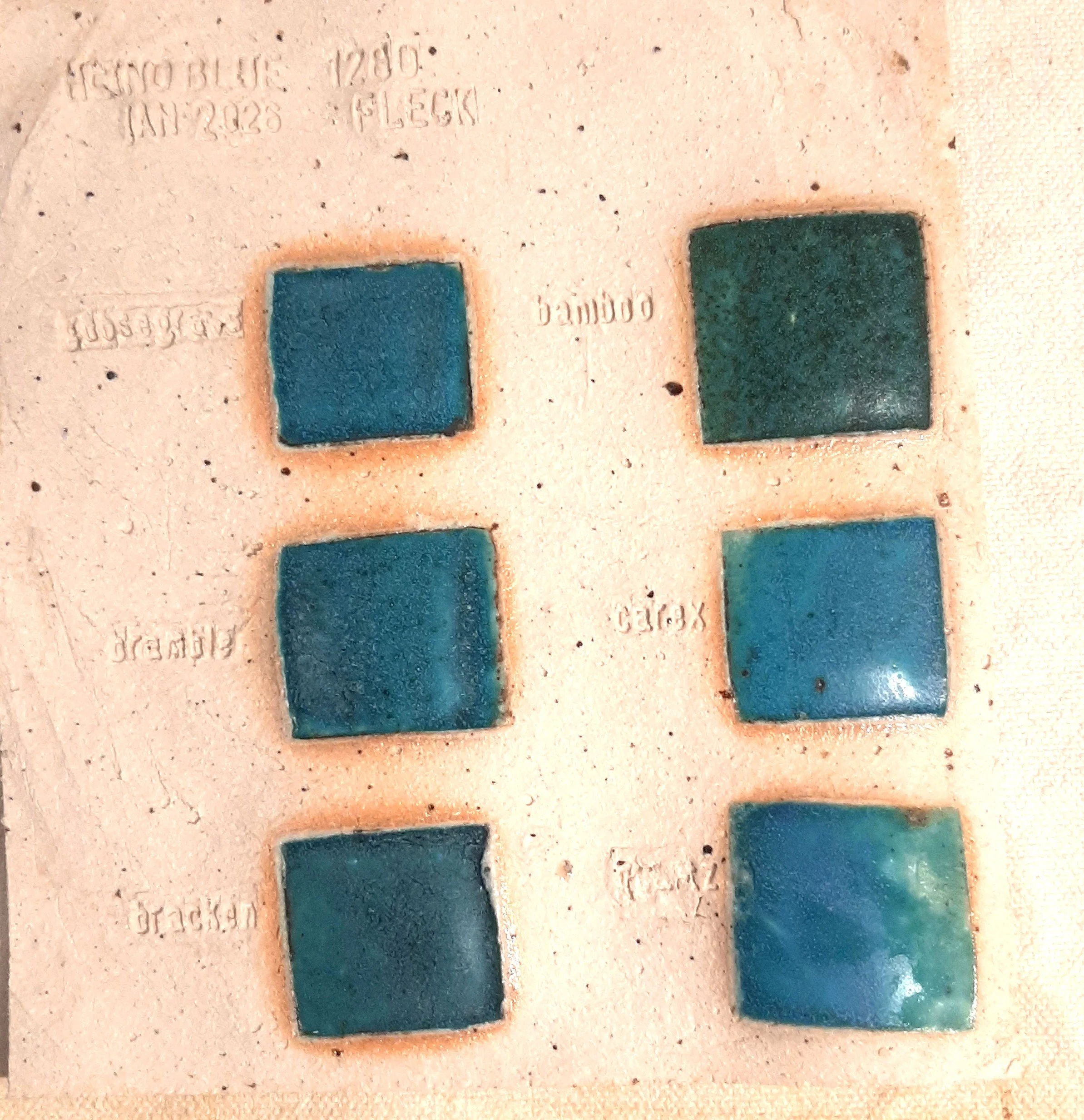 A close-up of a textured surface featuring blue, green, and turquoise square stickers with embossed text, some of which are difficult to read.