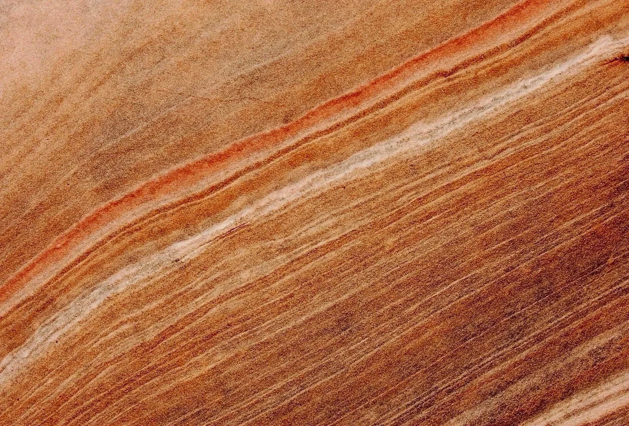 Close-up photo of layered sandstone rock with reddish-brown, orange, and white bands.