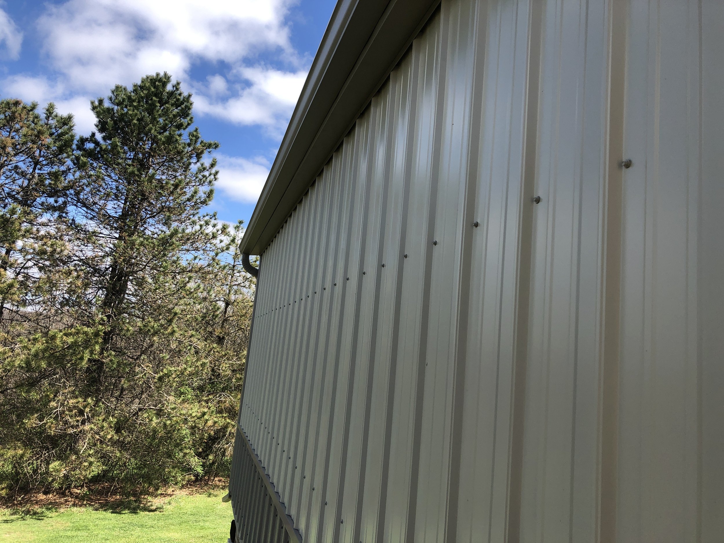 Close-up of a beige metal building siding with trees and blue sky in the background.