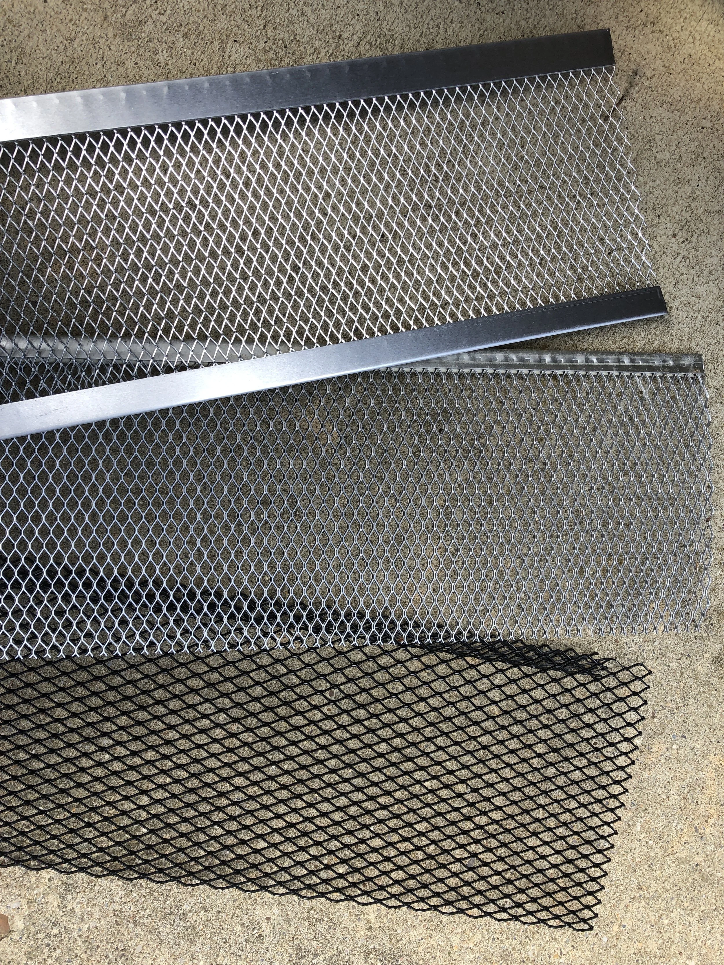 Three metal mesh screens, one in black, one in silver, and a third in silver with a bent edge, placed on a concrete surface.