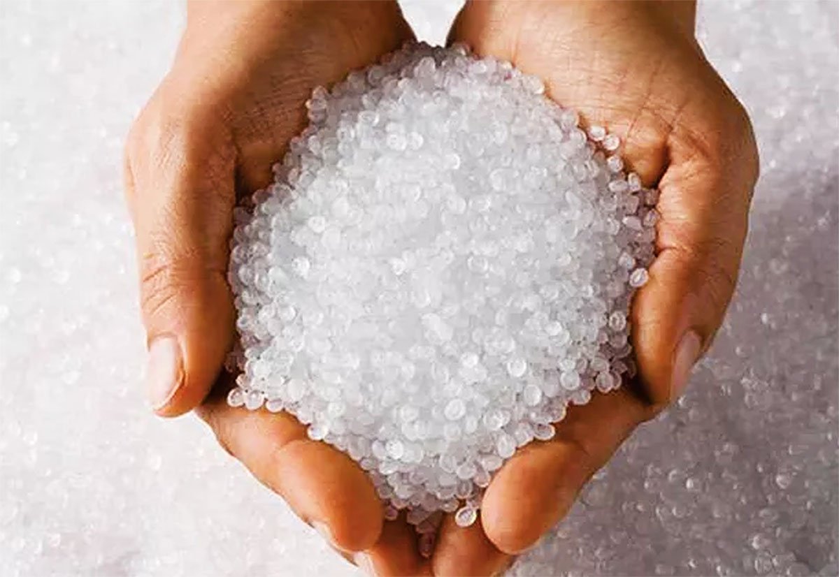 A hand holding a large handful of translucent white beads or granules, with more beads scattered on a surface in the background.