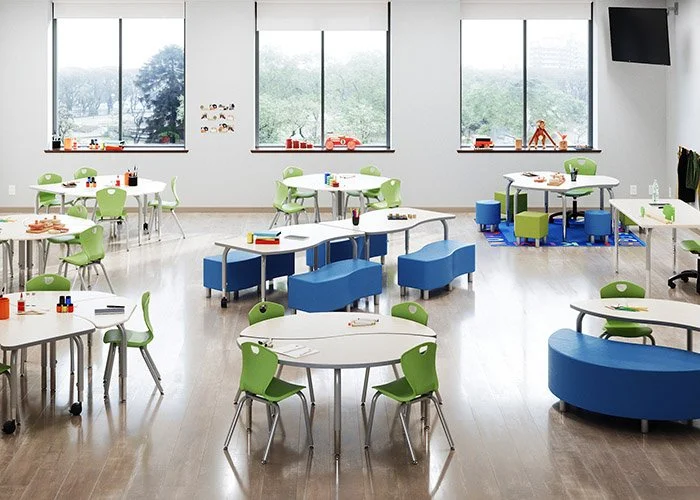 Classroom with round tables, green and blue chairs, and large windows.