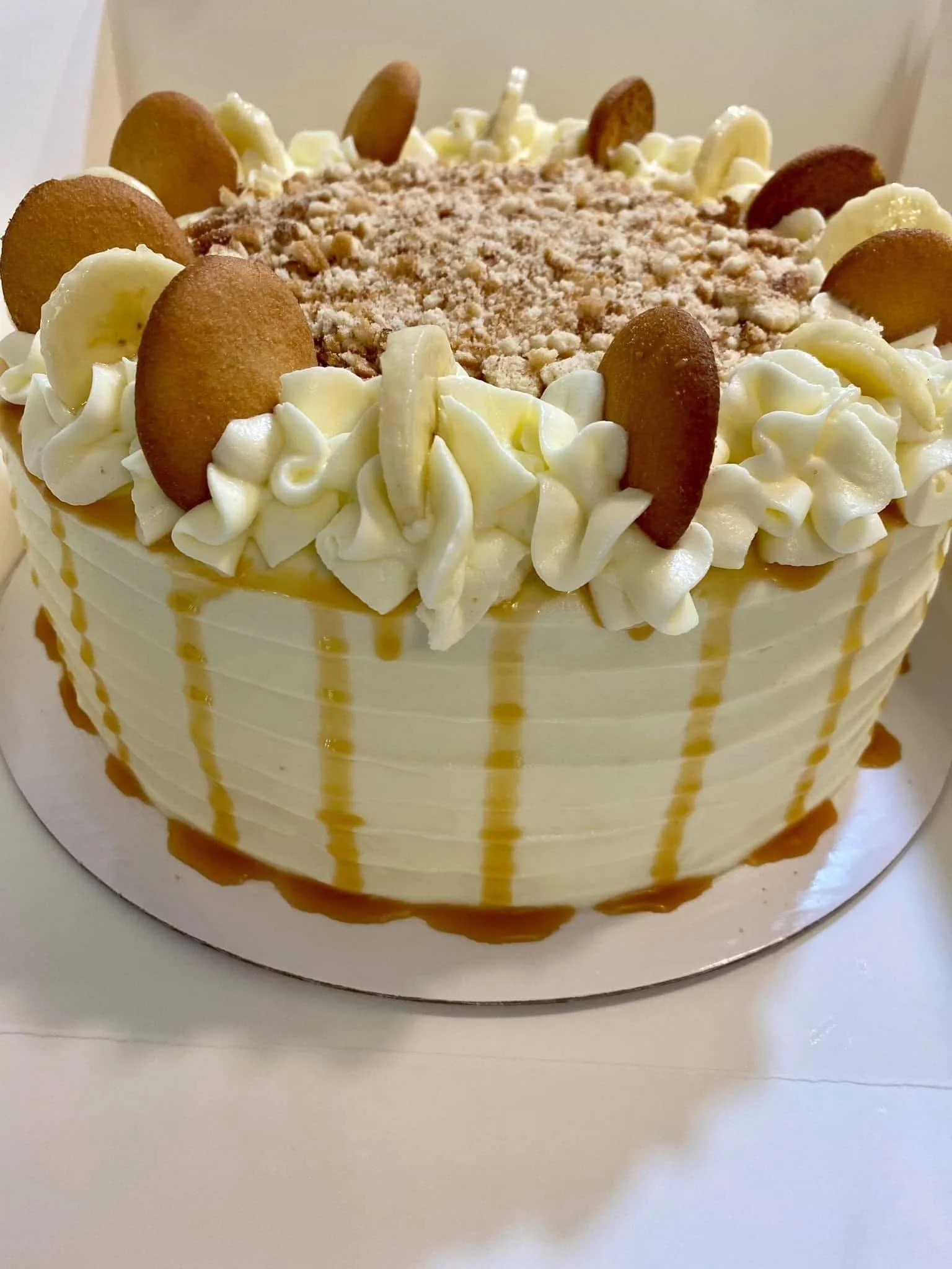 A layered cake with white frosting, caramel drizzle, white and brown cookies on top, and white piping around the edges.