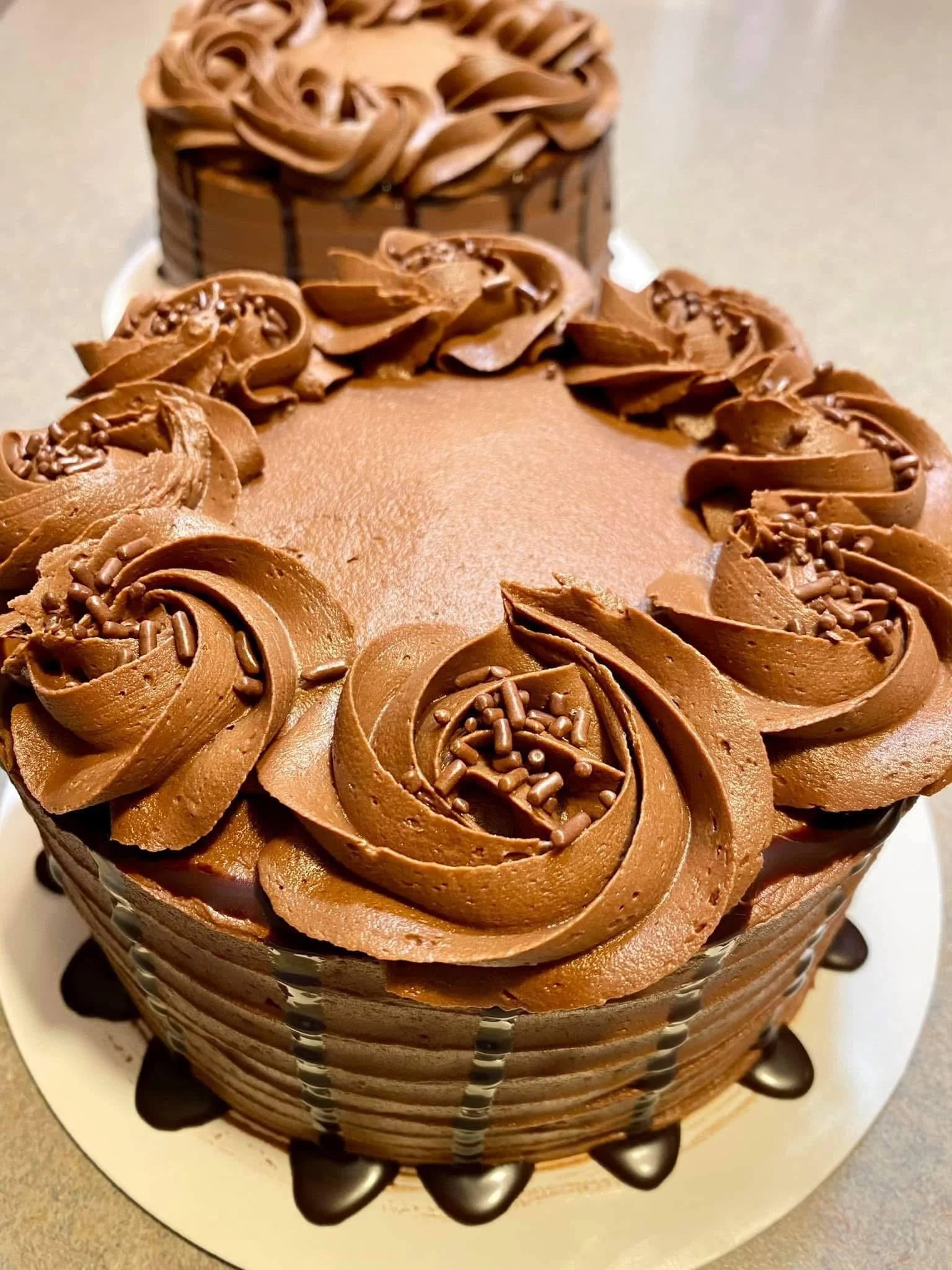 A chocolate cake decorated with swirls of chocolate frosting and chocolate sprinkles on top.