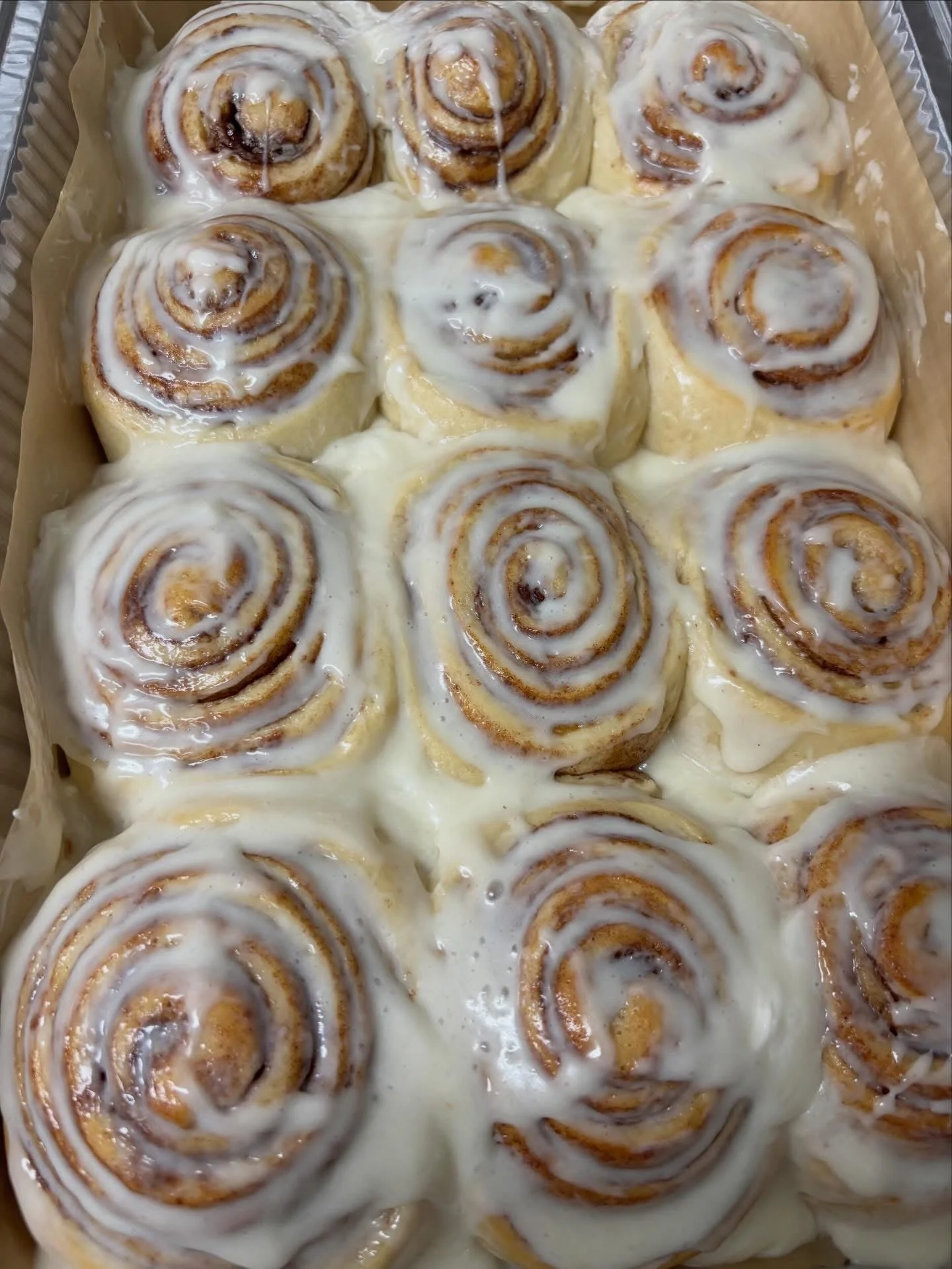 Baking tray with cinnamon rolls topped with cream cheese frosting.