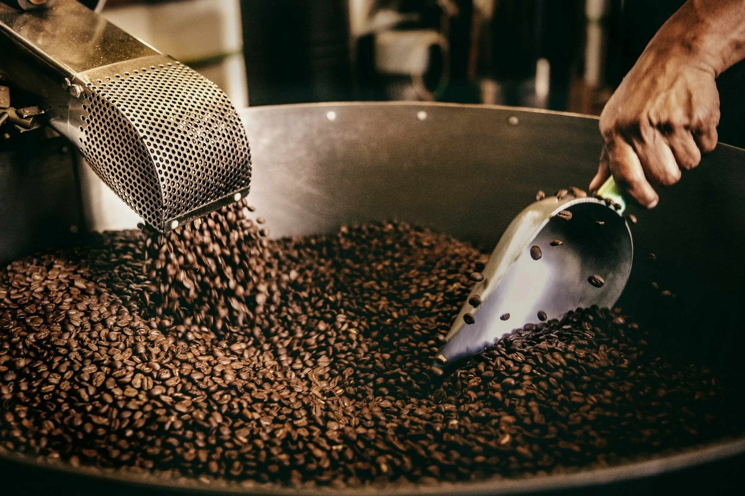 Una mano que manipula granos de café en una máquina de tostado.