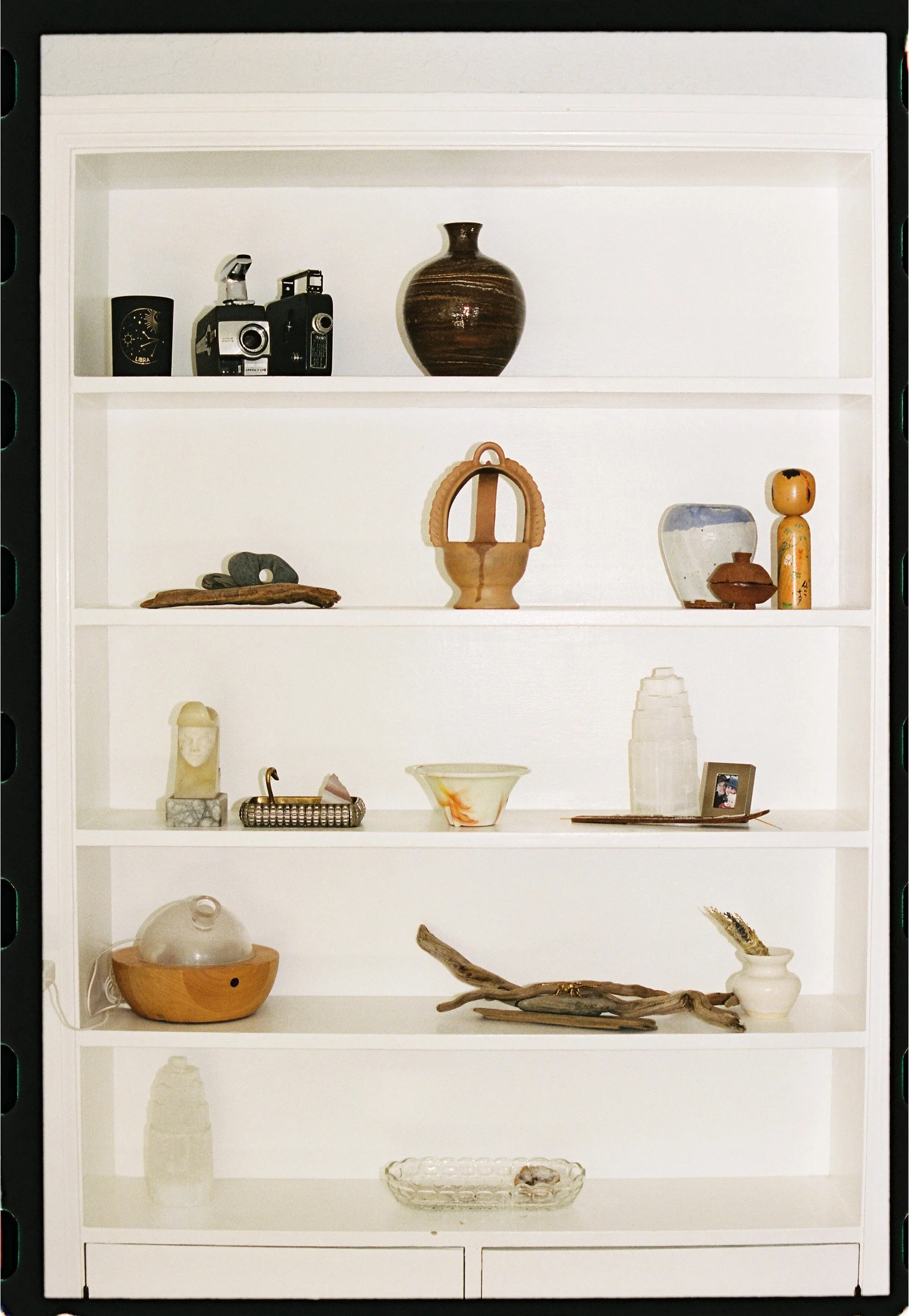 White bookshelf with various decorative items, including pottery, small sculptures, a framed photo, and a glass bowl.