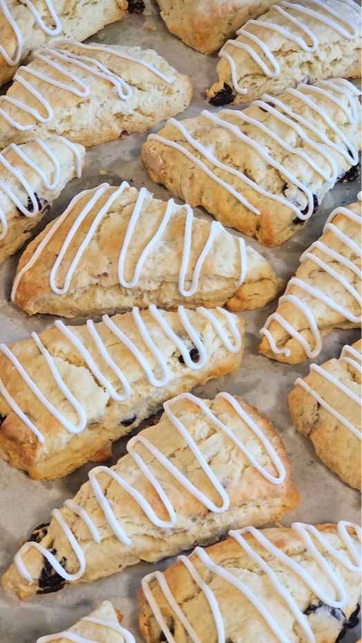 A tray of freshly baked scones with white icing drizzle and dried fruit bits.