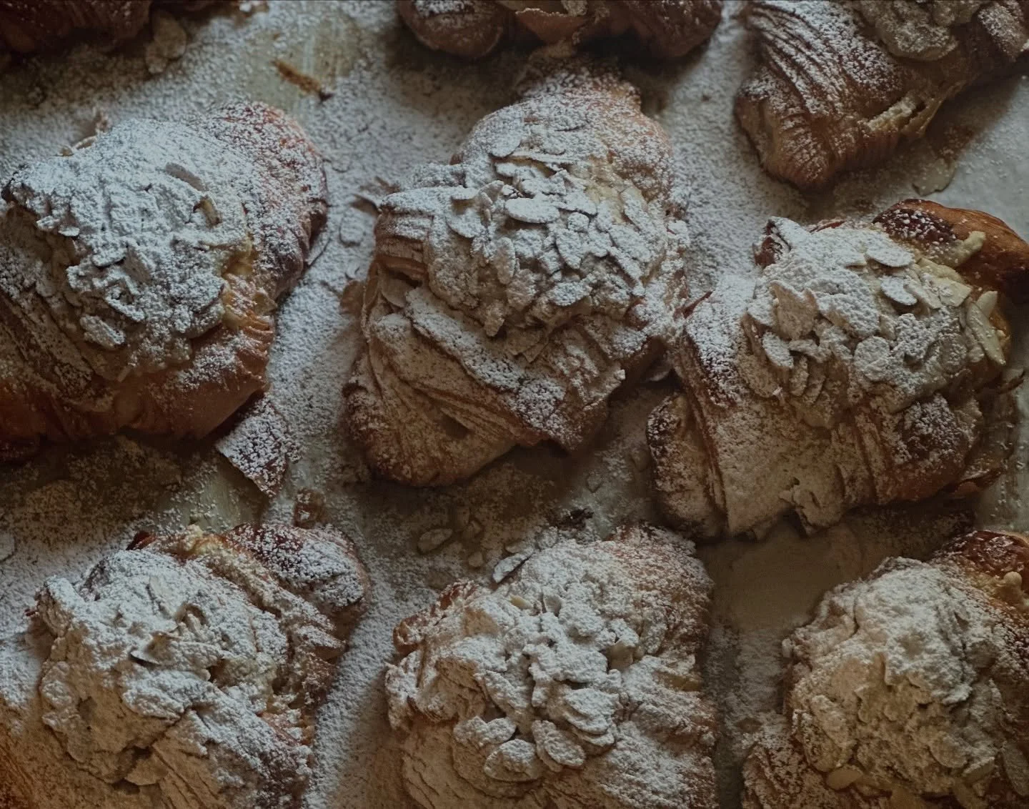 Several croissants topped with sliced almonds and powdered sugar.
