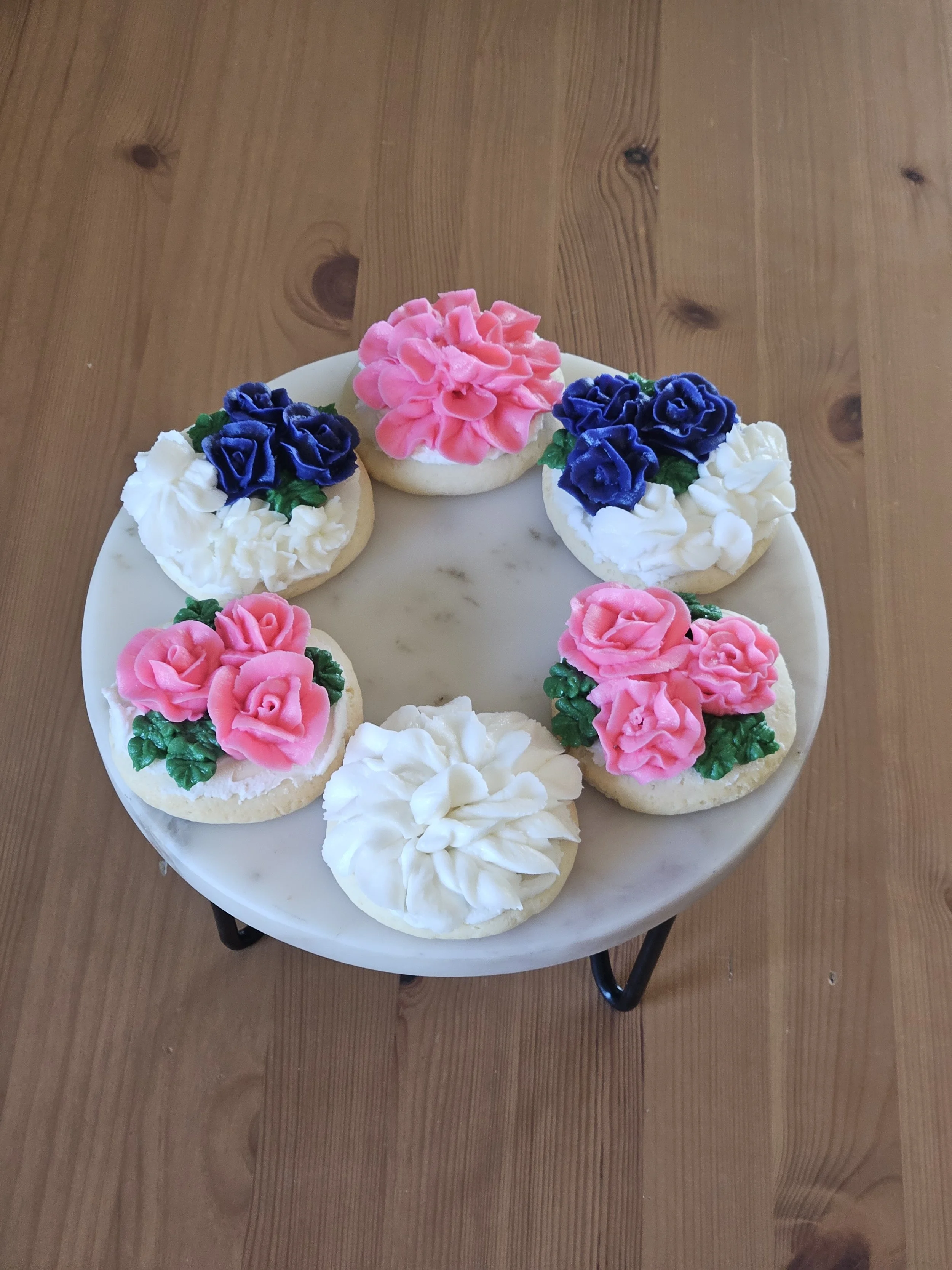 Decorative cookies with pink and purple flower icing on a white plate.