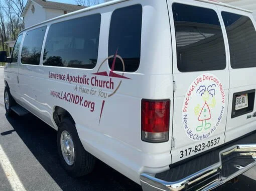 White church van with red lettering advertising Lawrence Apostolic Church and website, along with a logo of a slice of cake with a cherry, and a phone number.