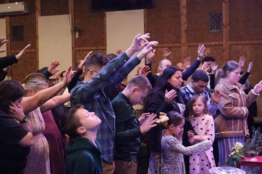 Group of people praying with hands raised in a church or religious setting.