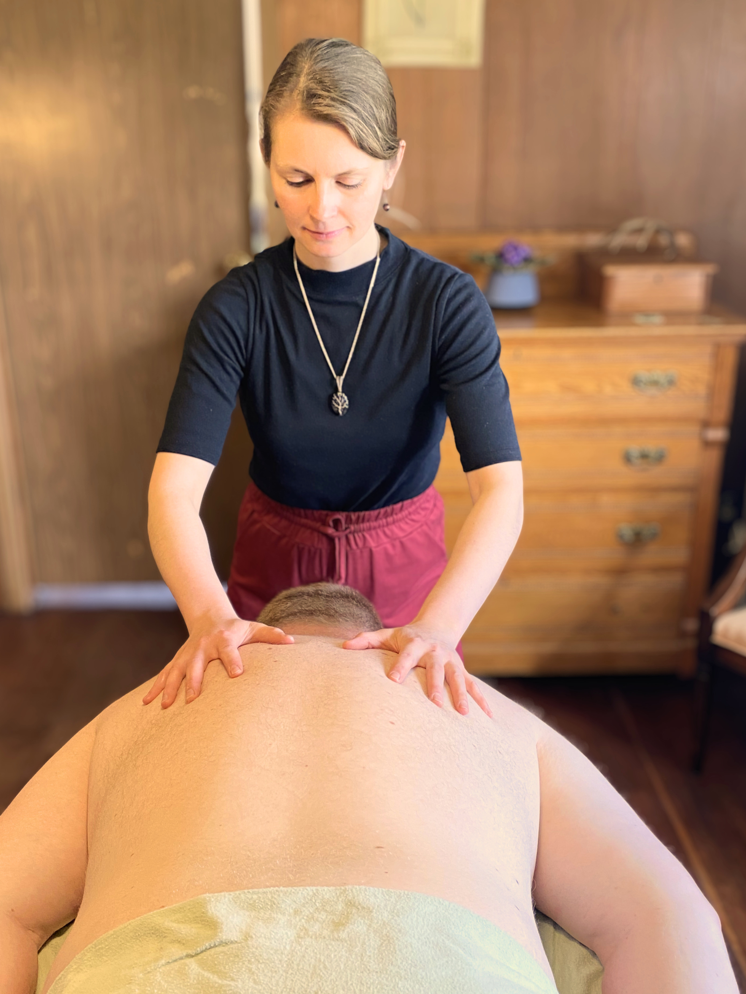 A woman giving myofascial release and energetic reset of the body to a man lying face down on a massage table in a massage room.