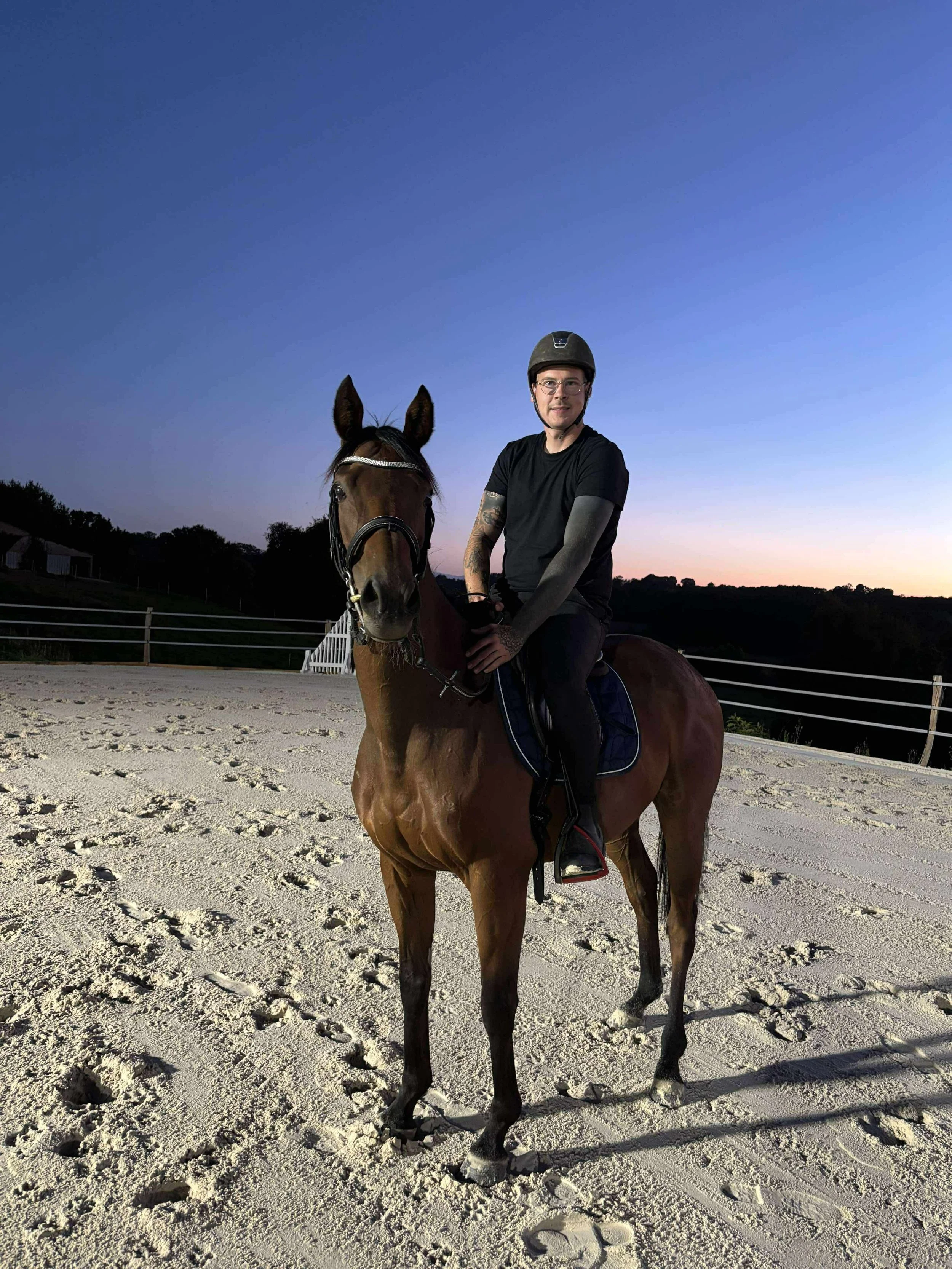 Homme à cheval, portant un casque, pendant le crépuscule dans une carrière équestre.