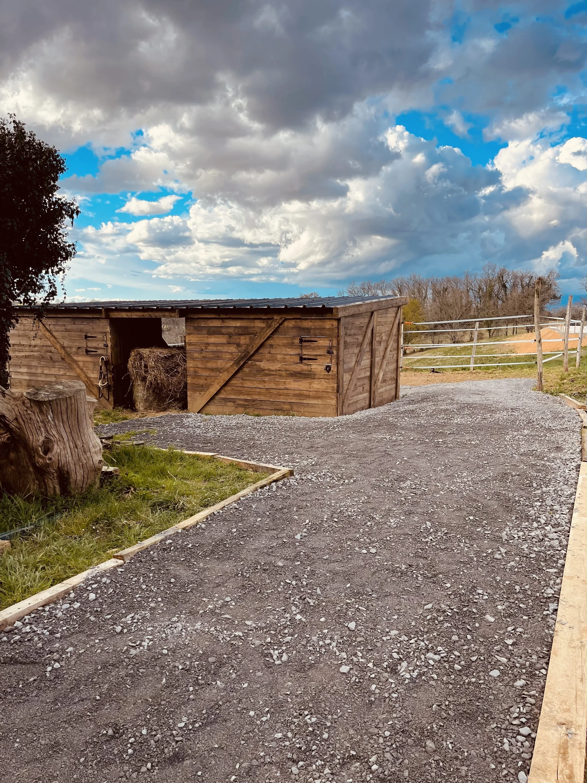 Un abri en bois sur un chemin de gravier, avec un ciel nuageux et un horizon rural
