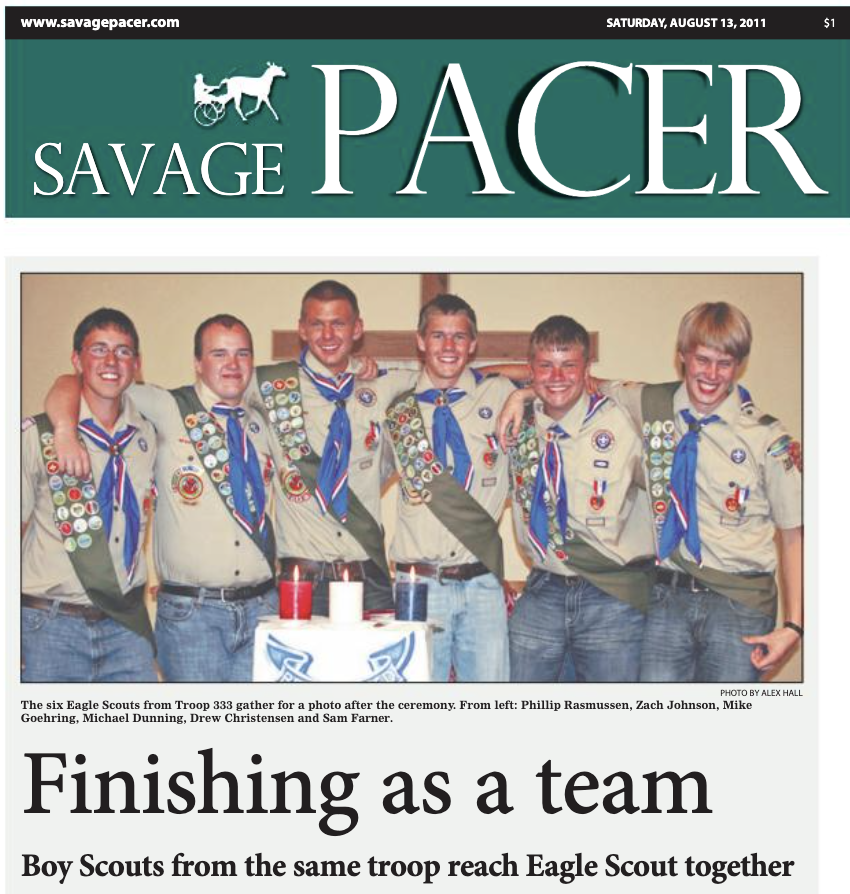 Group of six Boy Scouts in uniforms with merit badges, standing together indoors after a ceremony, with a table holding candles in front of them.