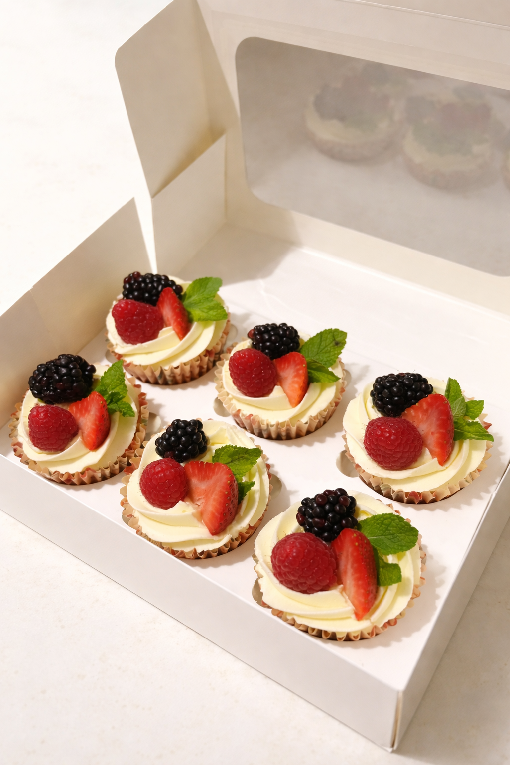 Box of vanilla buttercream cupcakes with fresh berries and mint