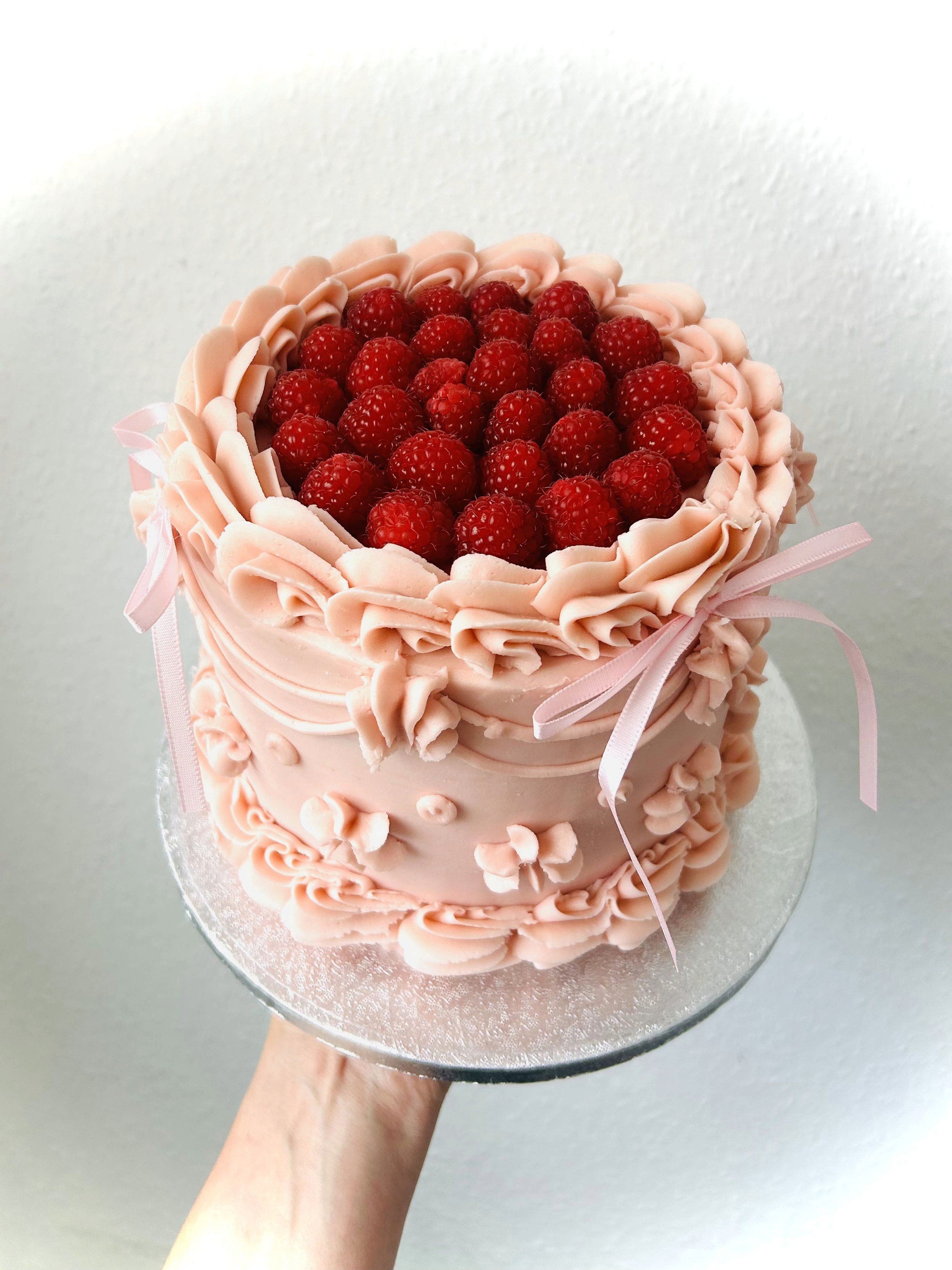 Pink buttercream cake with fresh raspberries and ribbon