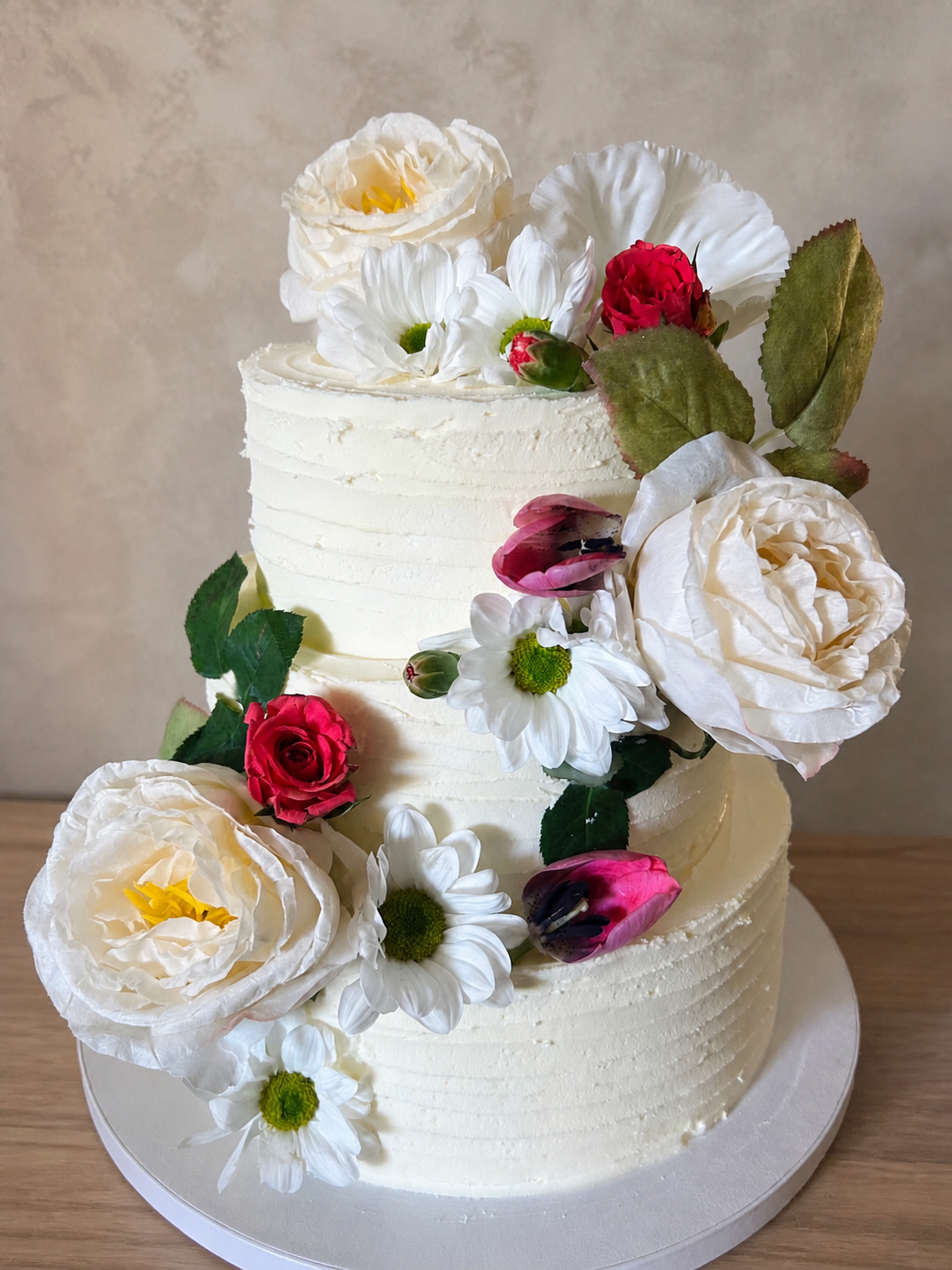 Three-tier white buttercream cake with fresh flowers