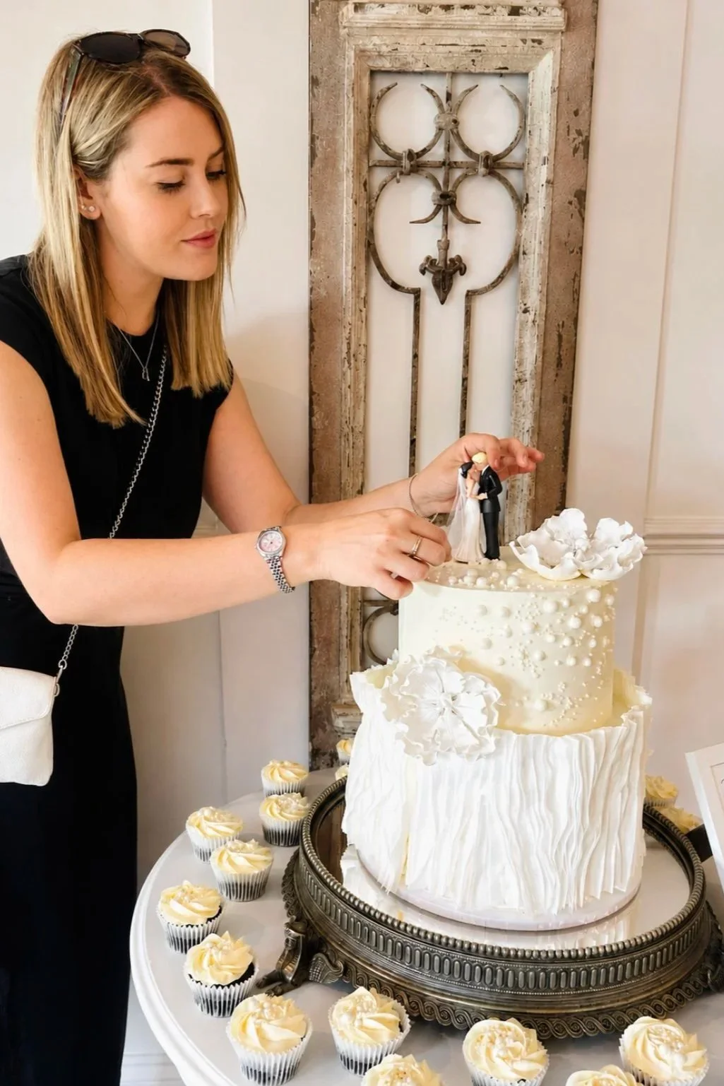 Isabelle Golder setting up a two-tier white wedding cake and cupcakes at a Woodhall Manor