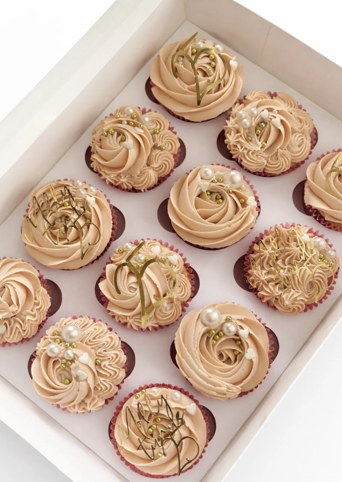 Box of buttercream cupcakes in soft peach, with pearl and gold decorations