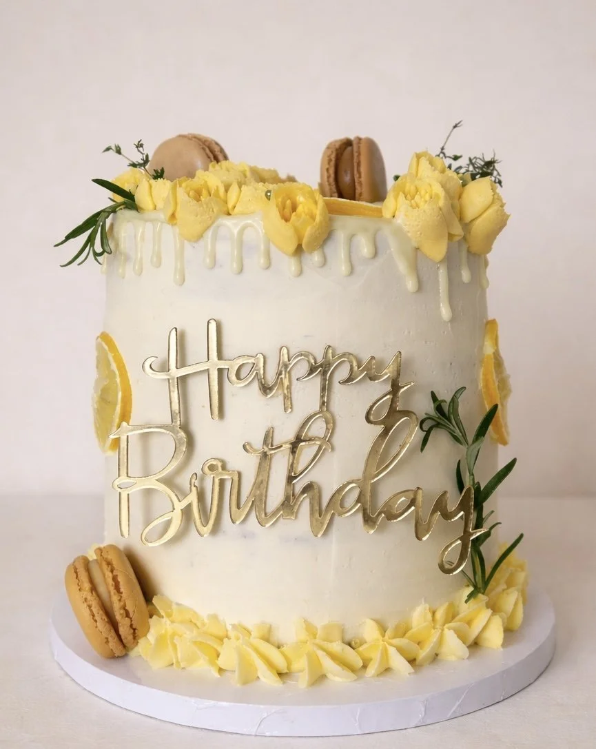 Buttercream birthday cake with yellow flowers, macarons and a gold Happy Birthday topper