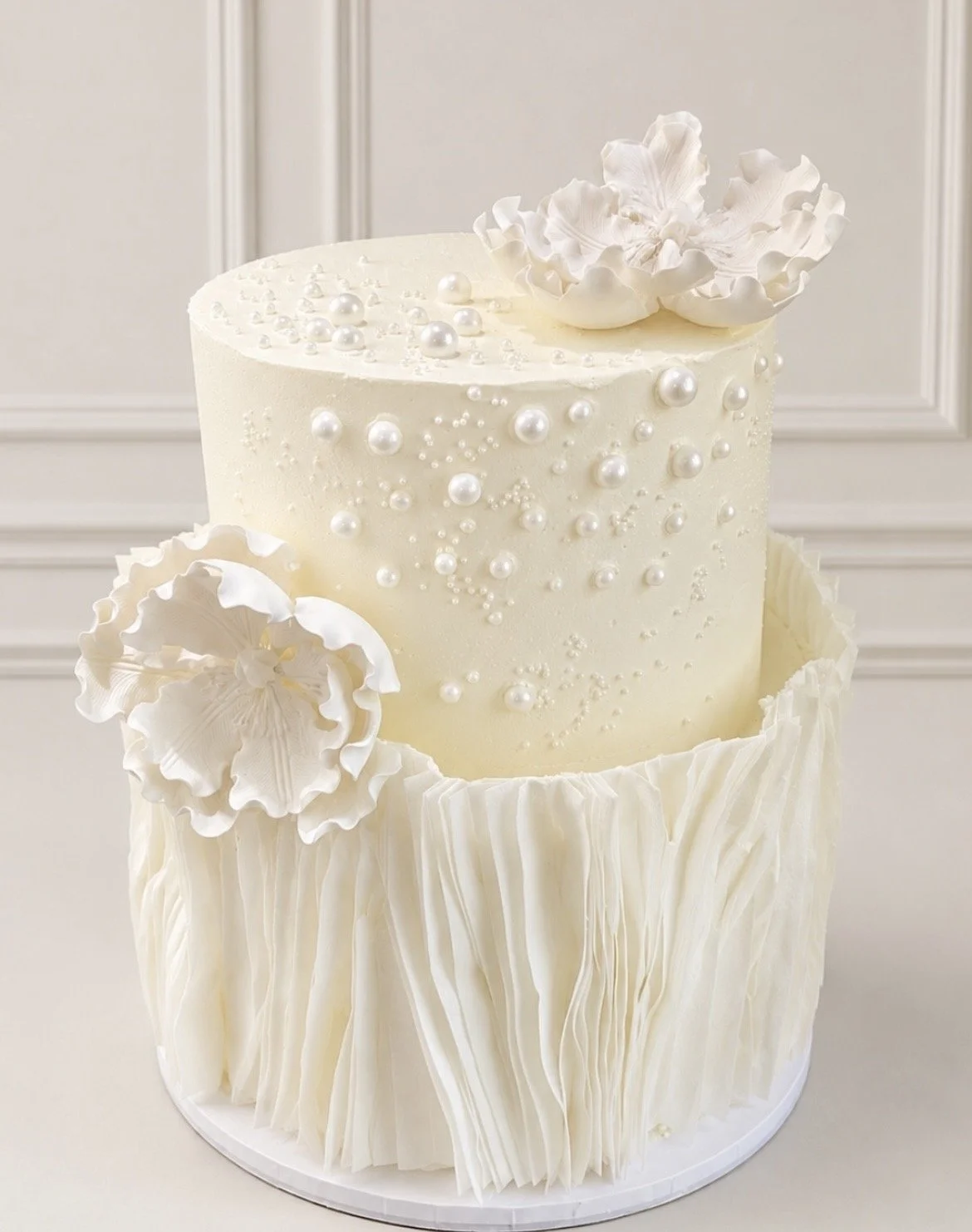 Two-tier white wedding cake with edible pearls, wafer paper and decorative flowers
