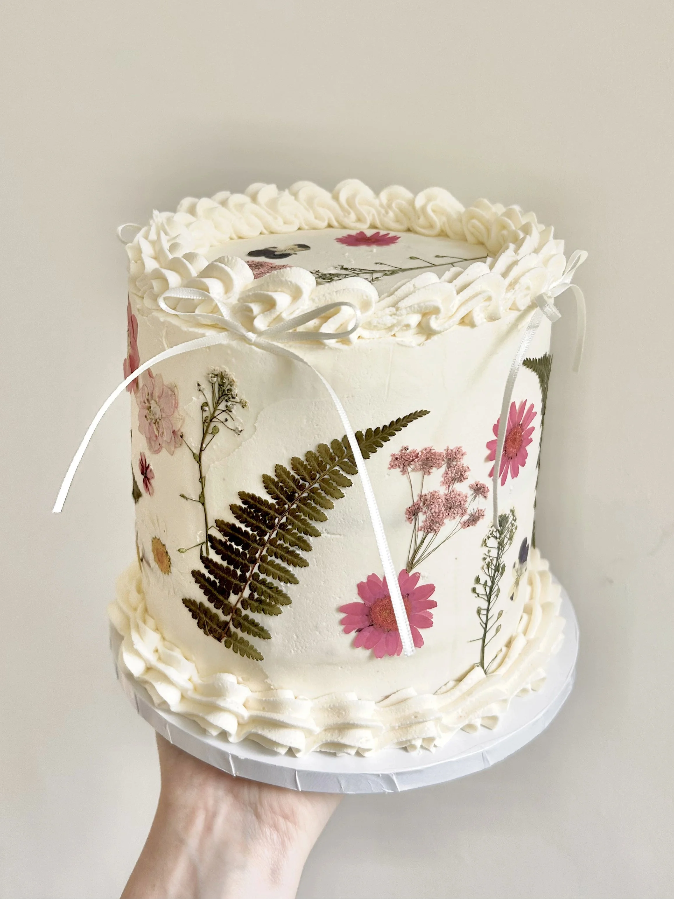 White buttercream cake with pressed flowers and ribbon