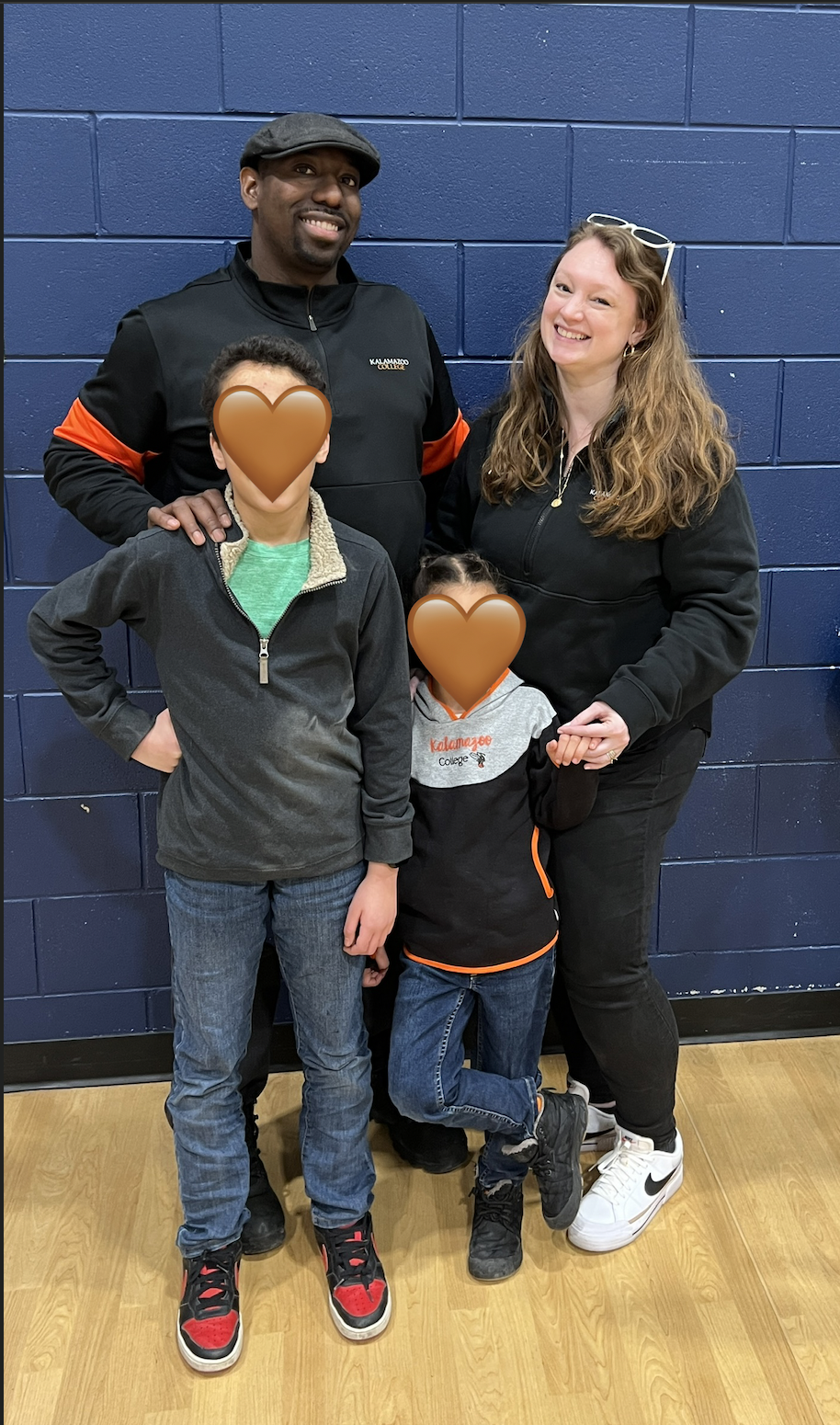 Caitlin's husband and kids (with faces covered for privacy) smile at the camera at a school event.