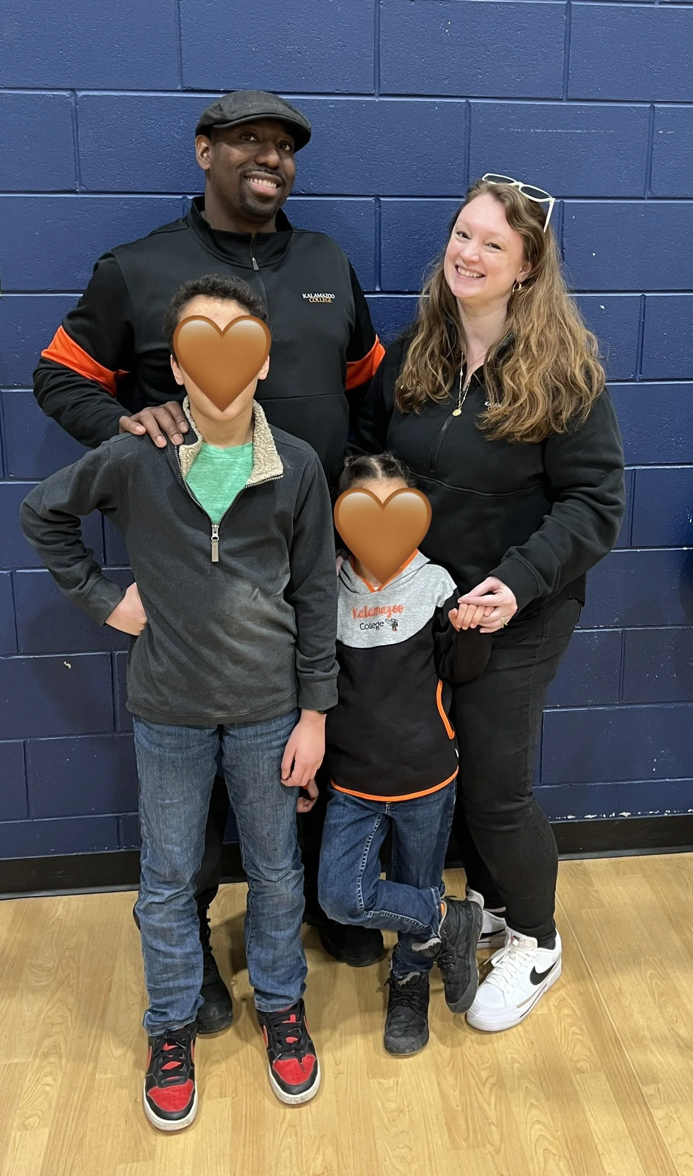 Caitlin poses in a school gym with her husband and children (whose faces are covered to protect their privacy and consent).