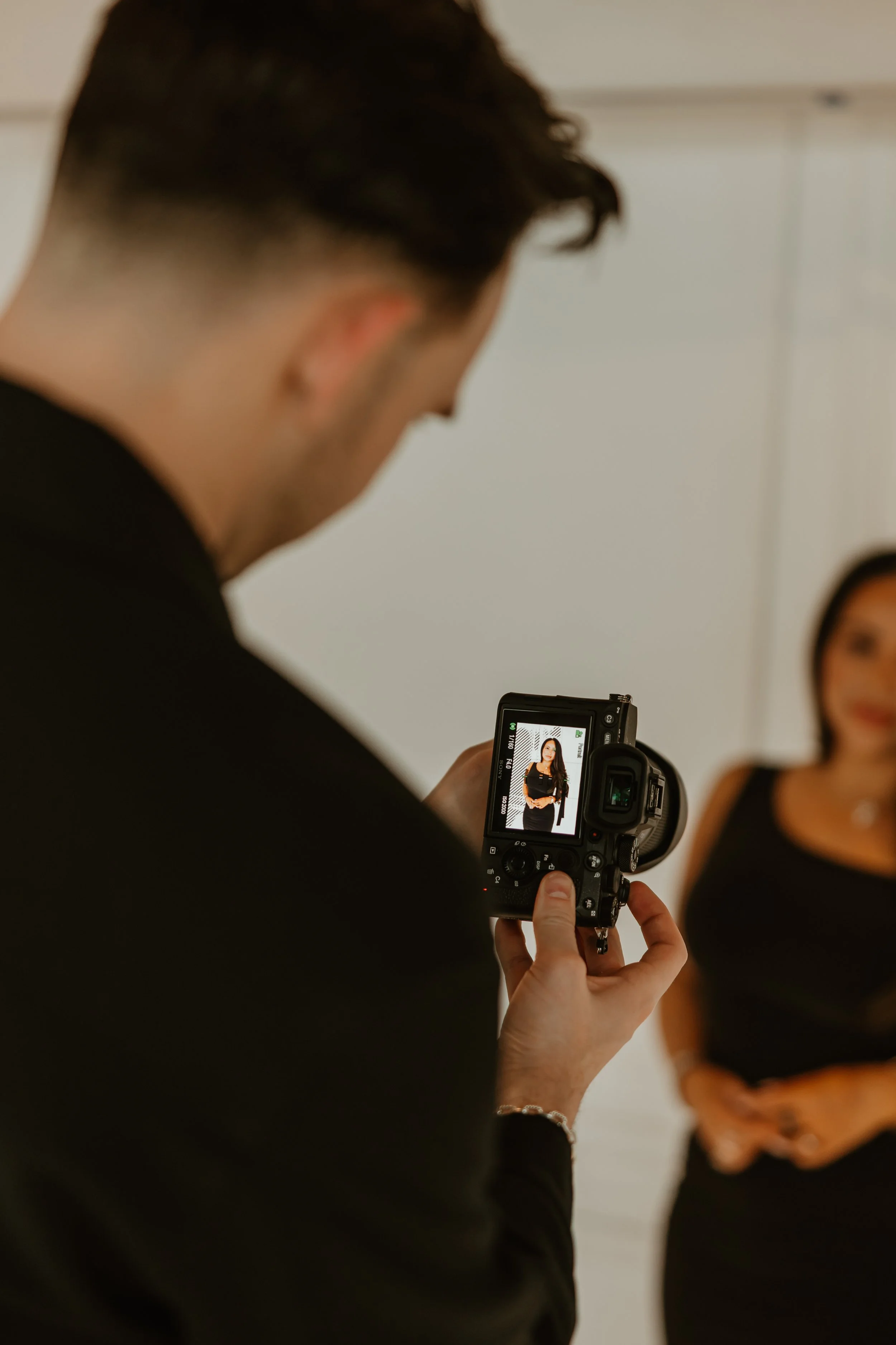 A man taking a photograph of a woman using a digital camera indoors.
