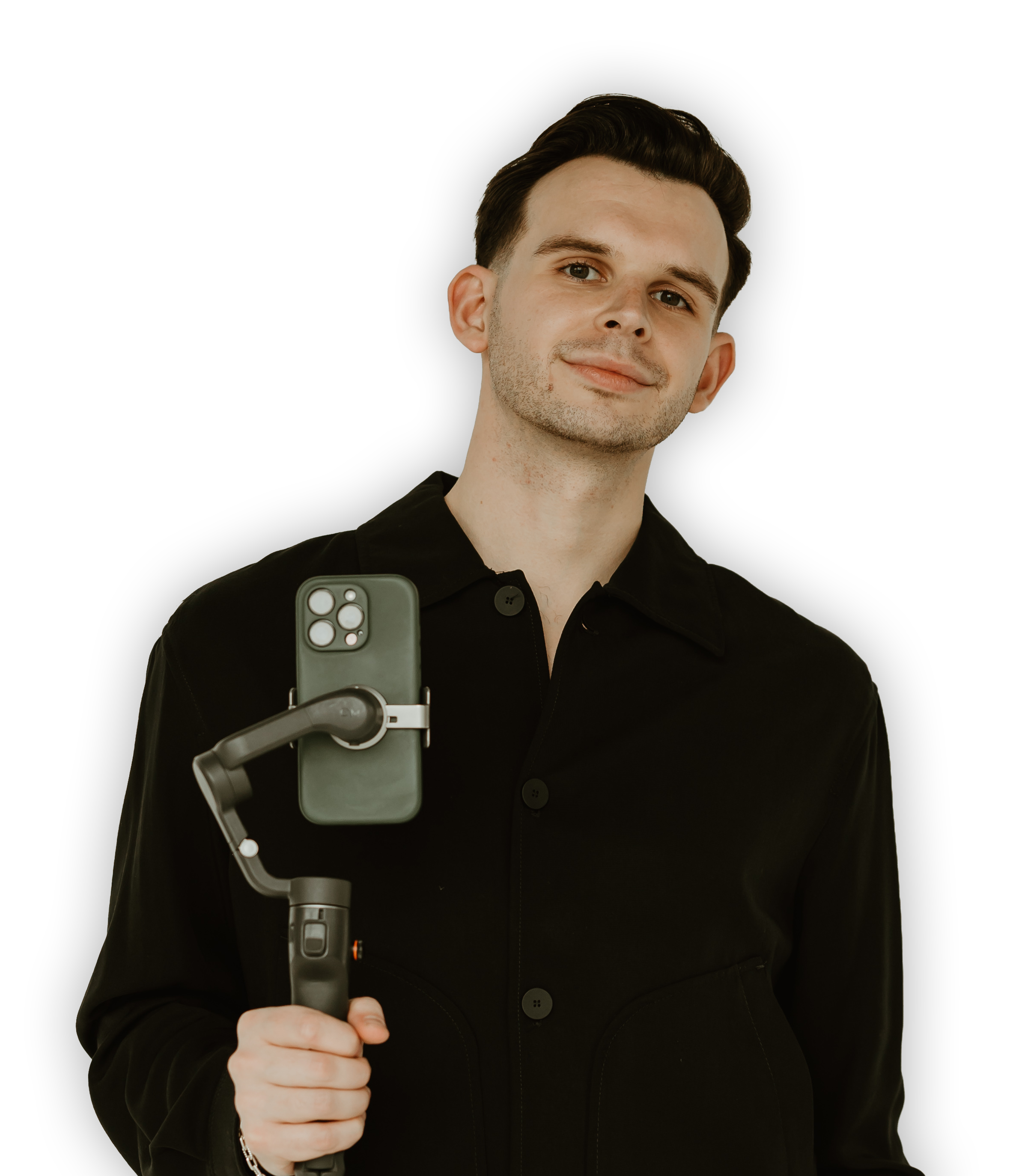 A young man with dark hair, wearing a black shirt, smiling and holding a handheld stabilizer with a smartphone attached.