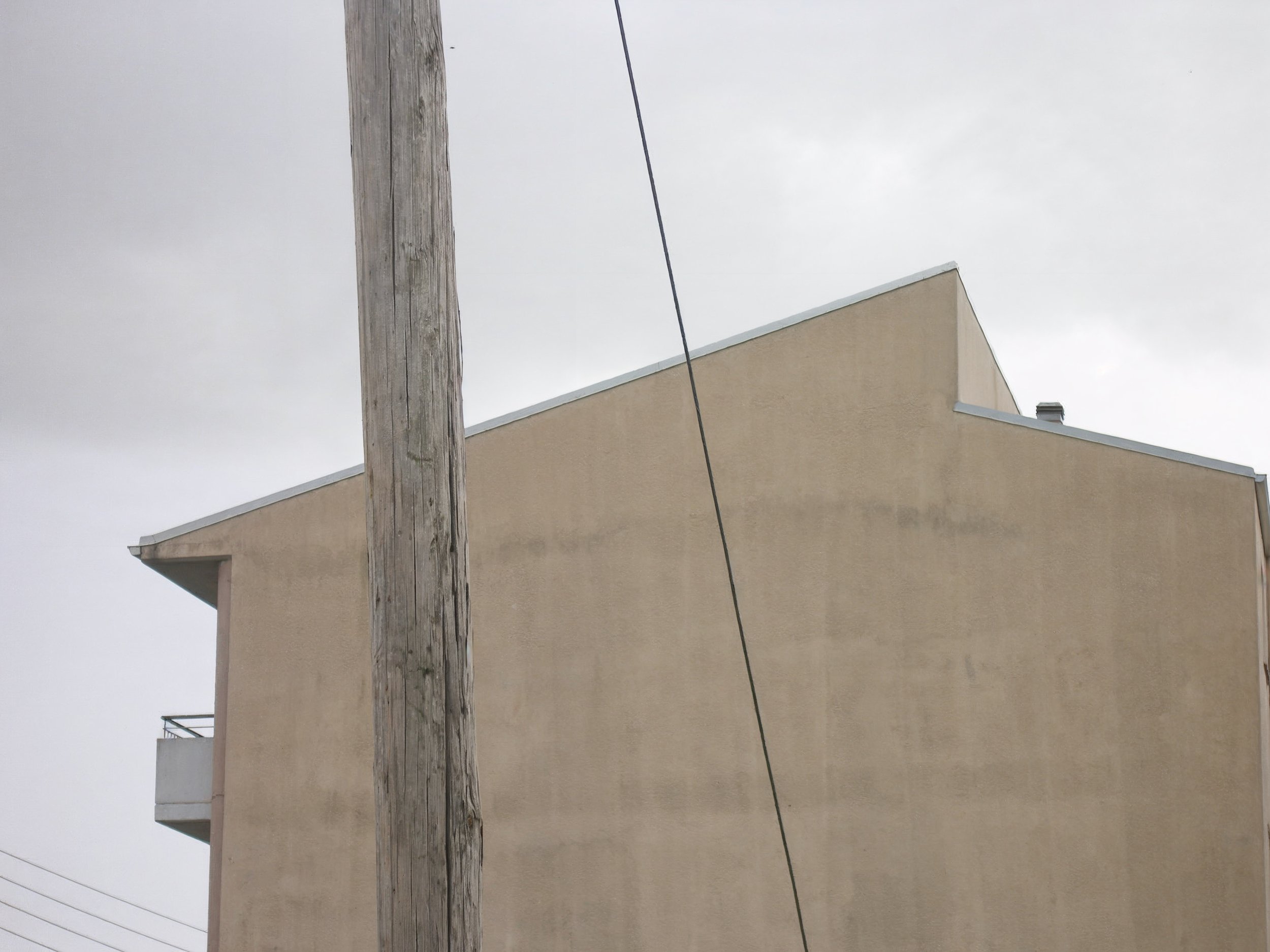 A beige building with a sloped roof and a chimney, partially obscured by a wooden utility pole with a diagonal wire, under a cloudy sky.