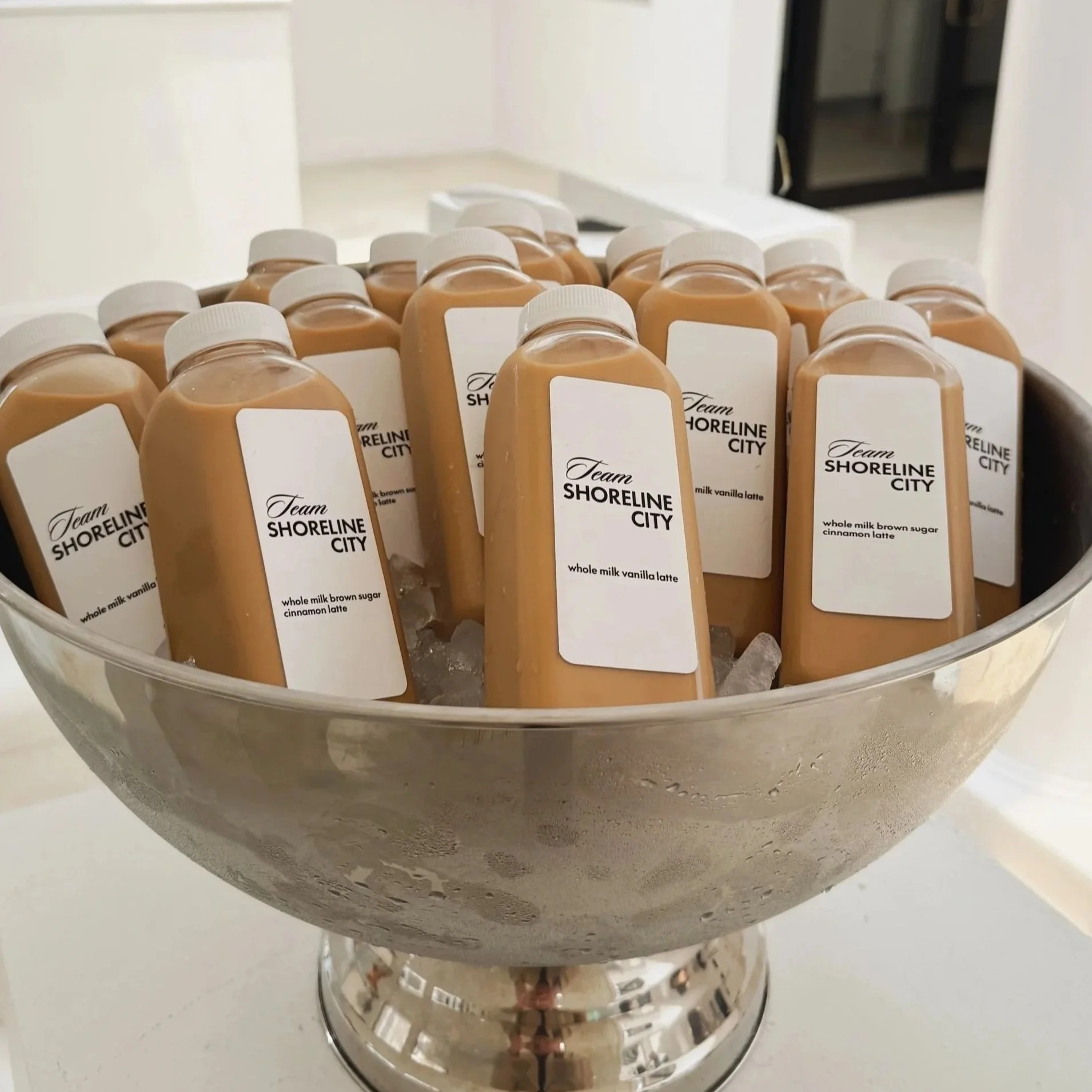 Bottles of Team Shoreline City vanilla latte drinks in a silver bowl on a white countertop.
