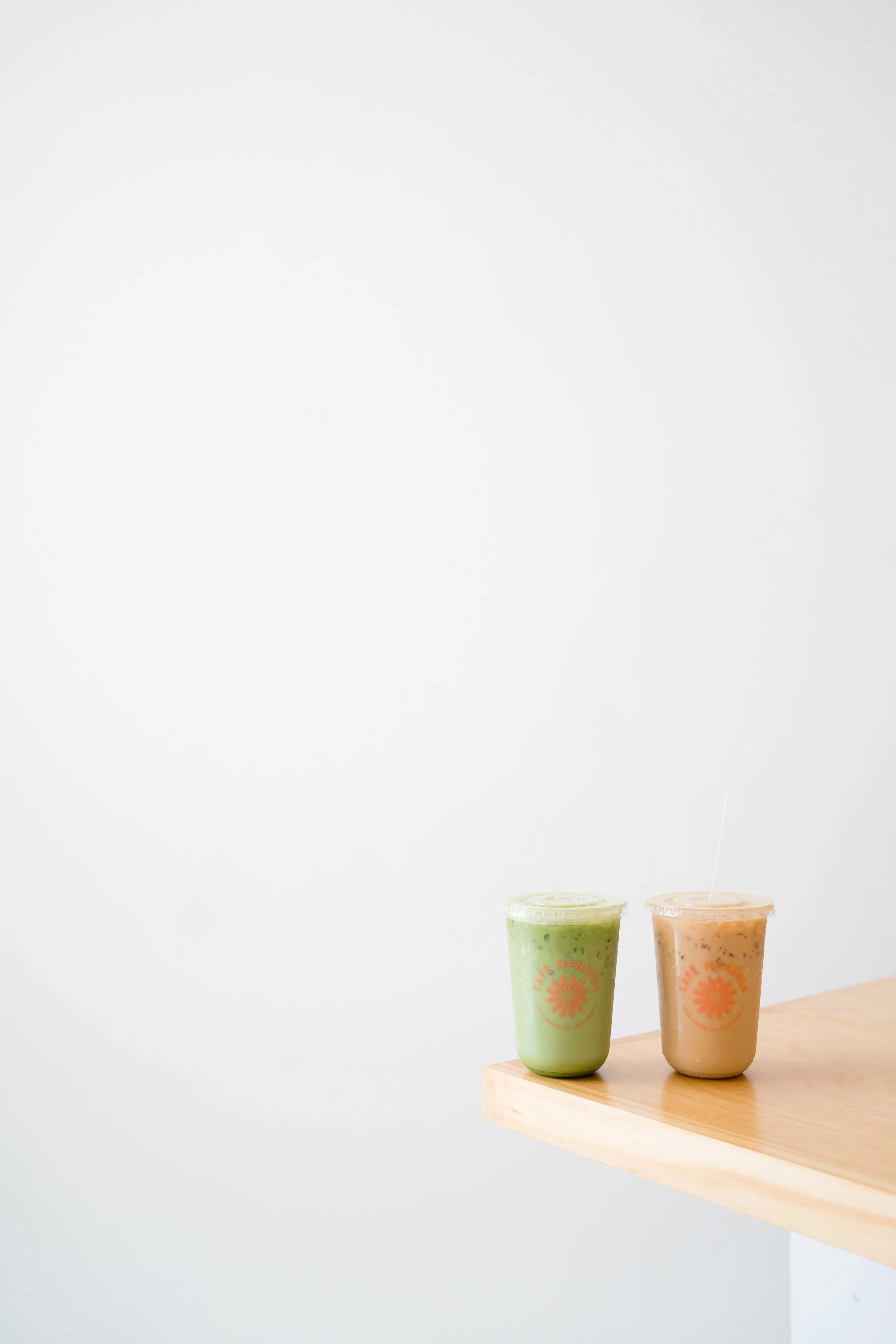 Two smoothies, one green and one light brown, on a wooden surface with a plain white background.
