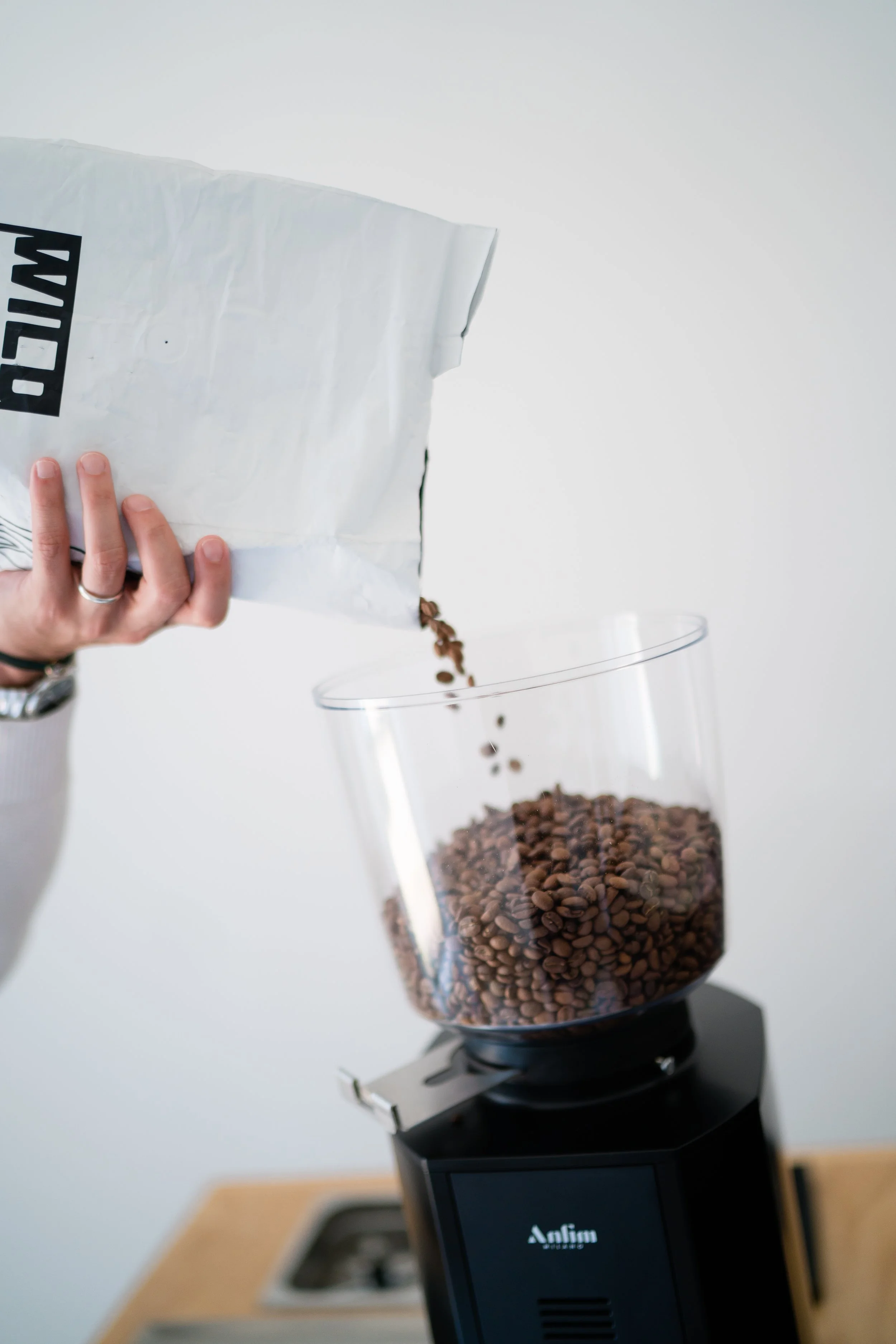 A person pouring coffee beans from a white bag into a coffee grinder.