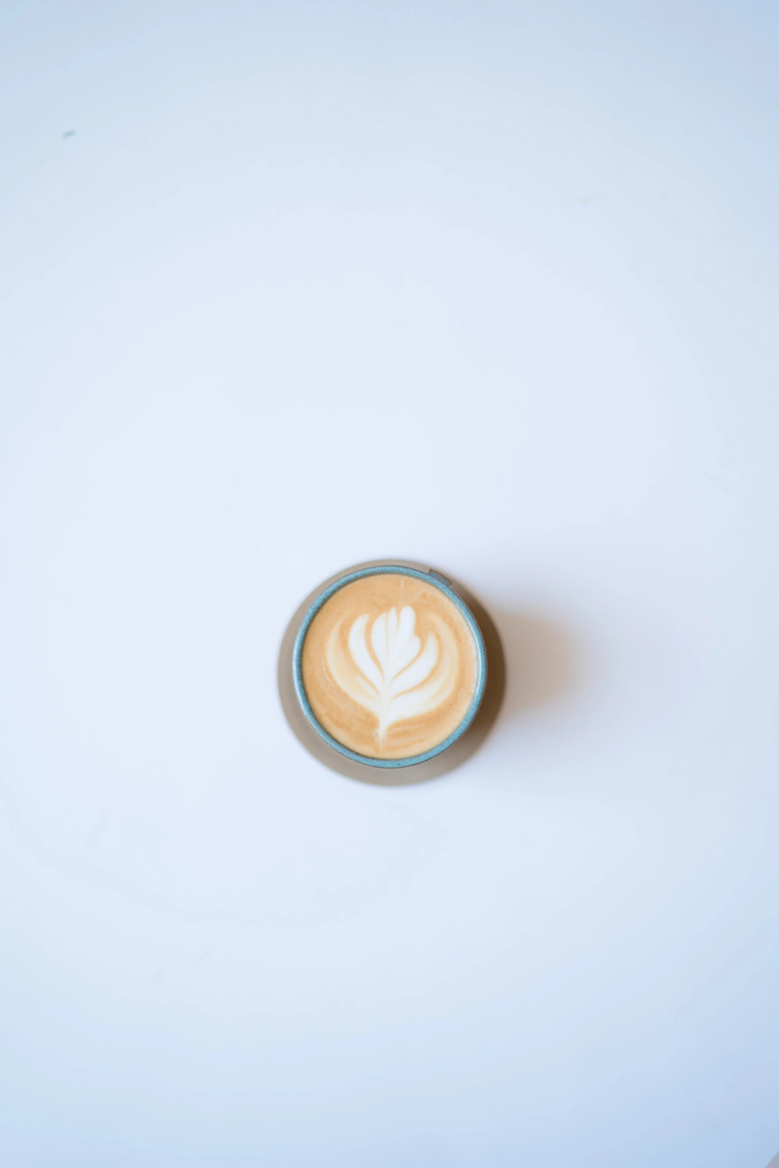 Top view of a latte with latte art in a ceramic cup placed on a white surface.