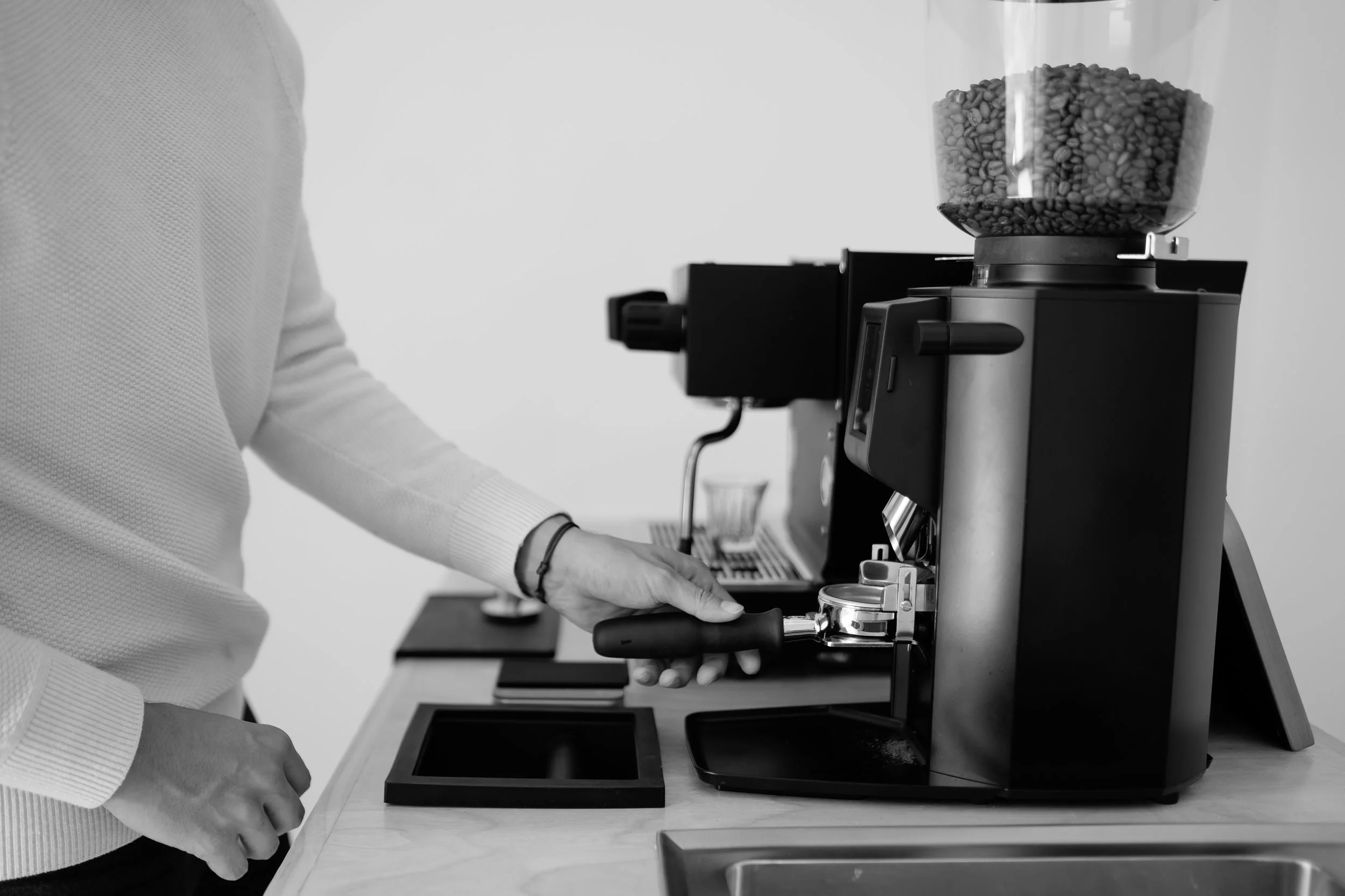 Person operating a coffee grinder machine, with coffee beans visible inside the hopper.