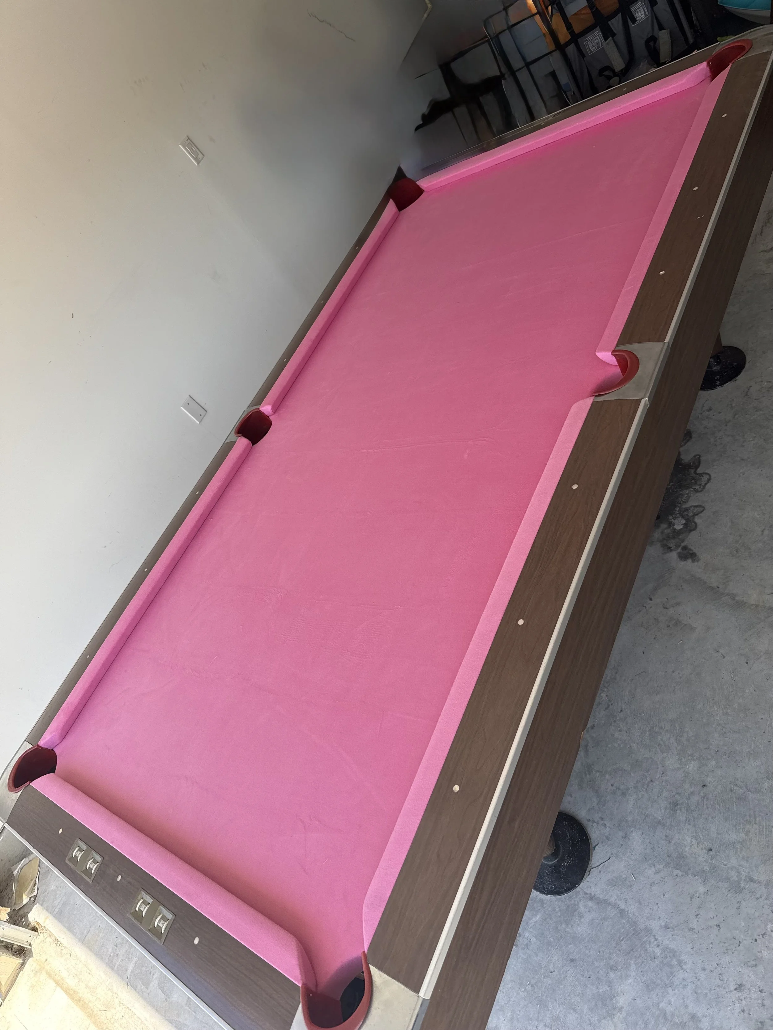 A pink billiards or pool table with a wooden frame, situated in a room with gray walls and a concrete floor.